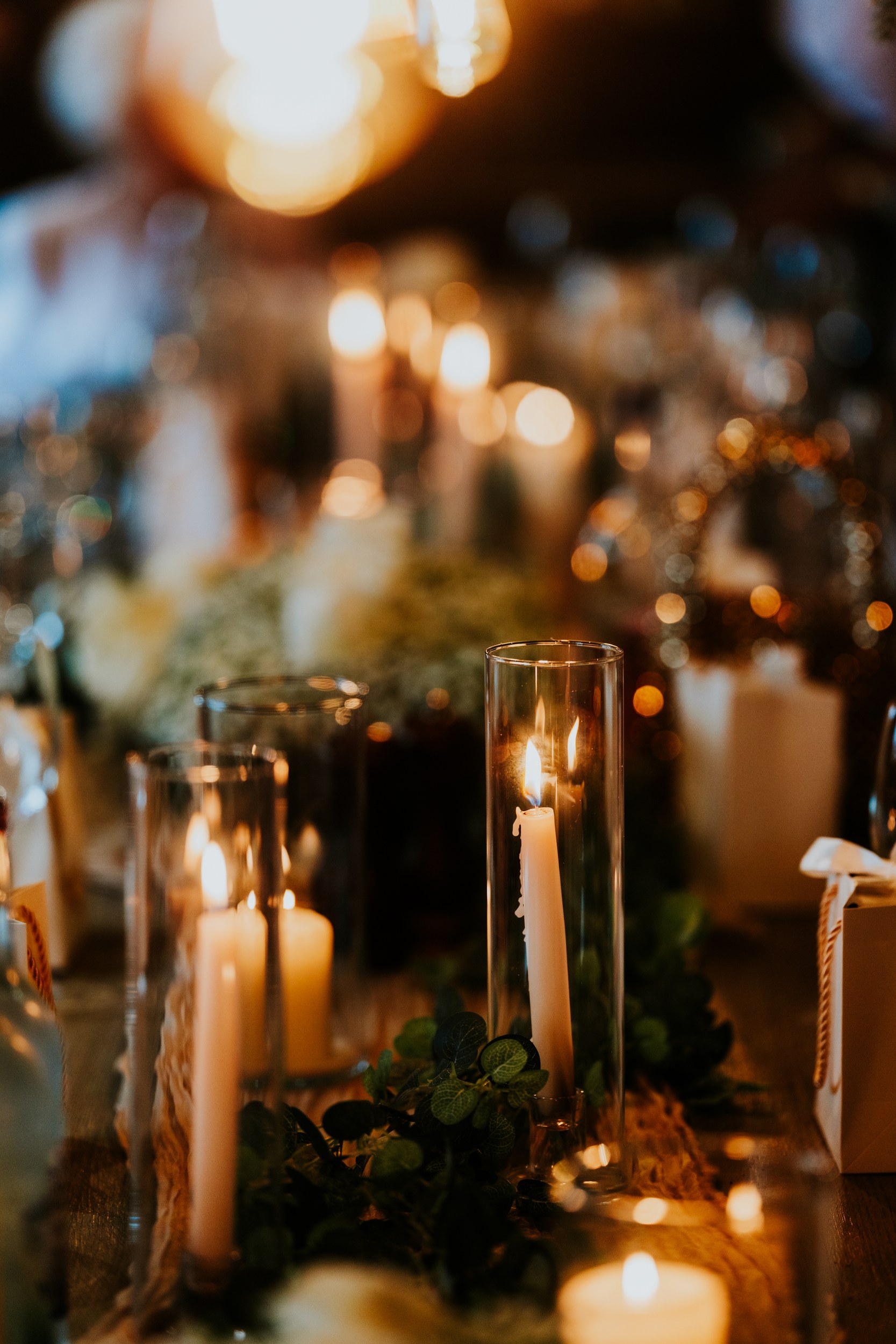Alana & Kyle’s Glasgow Wedding — City Centre to The Bothy 21 Close-up of lit taper candles in glass holders on a decorated reception table with warm blurred lights.