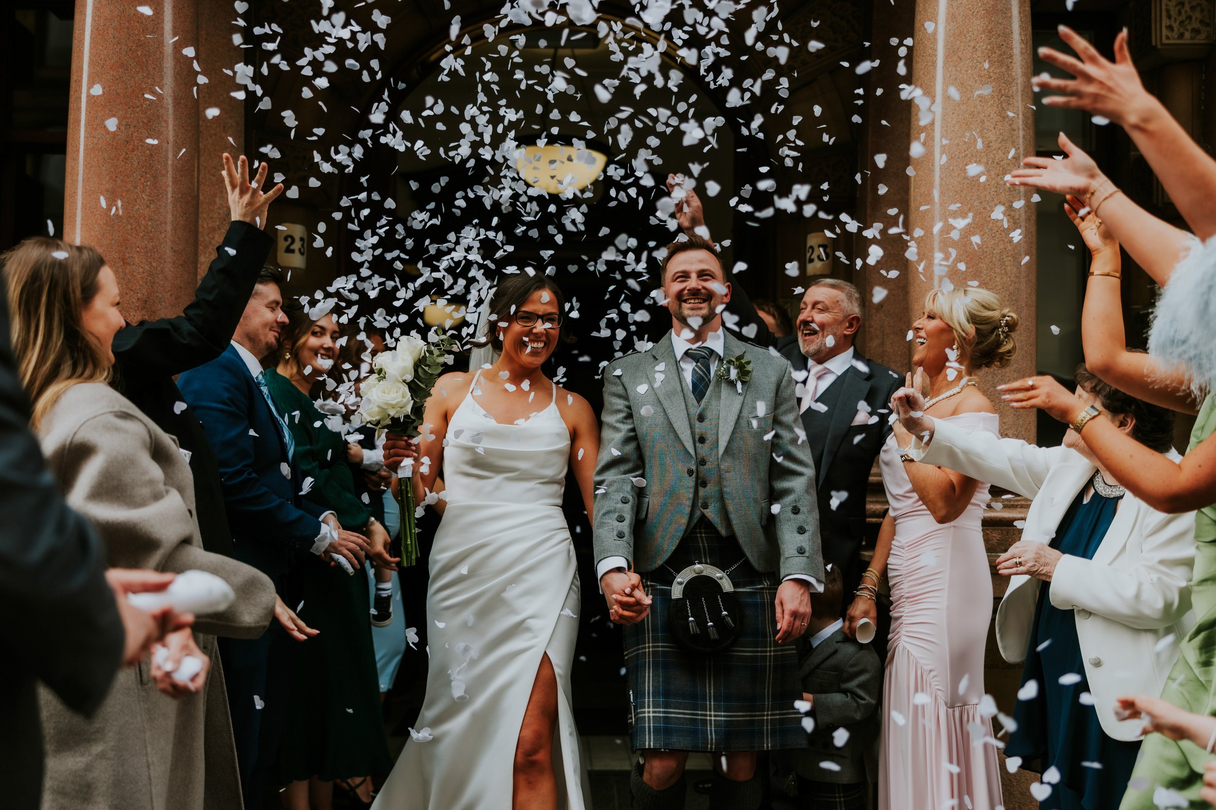 Alana & Kyle’s Glasgow Wedding — City Centre to The Bothy 8 Newlyweds leave the City Chambers under falling confetti, bride in white with bouquet and groom in kilt, guests cheering.