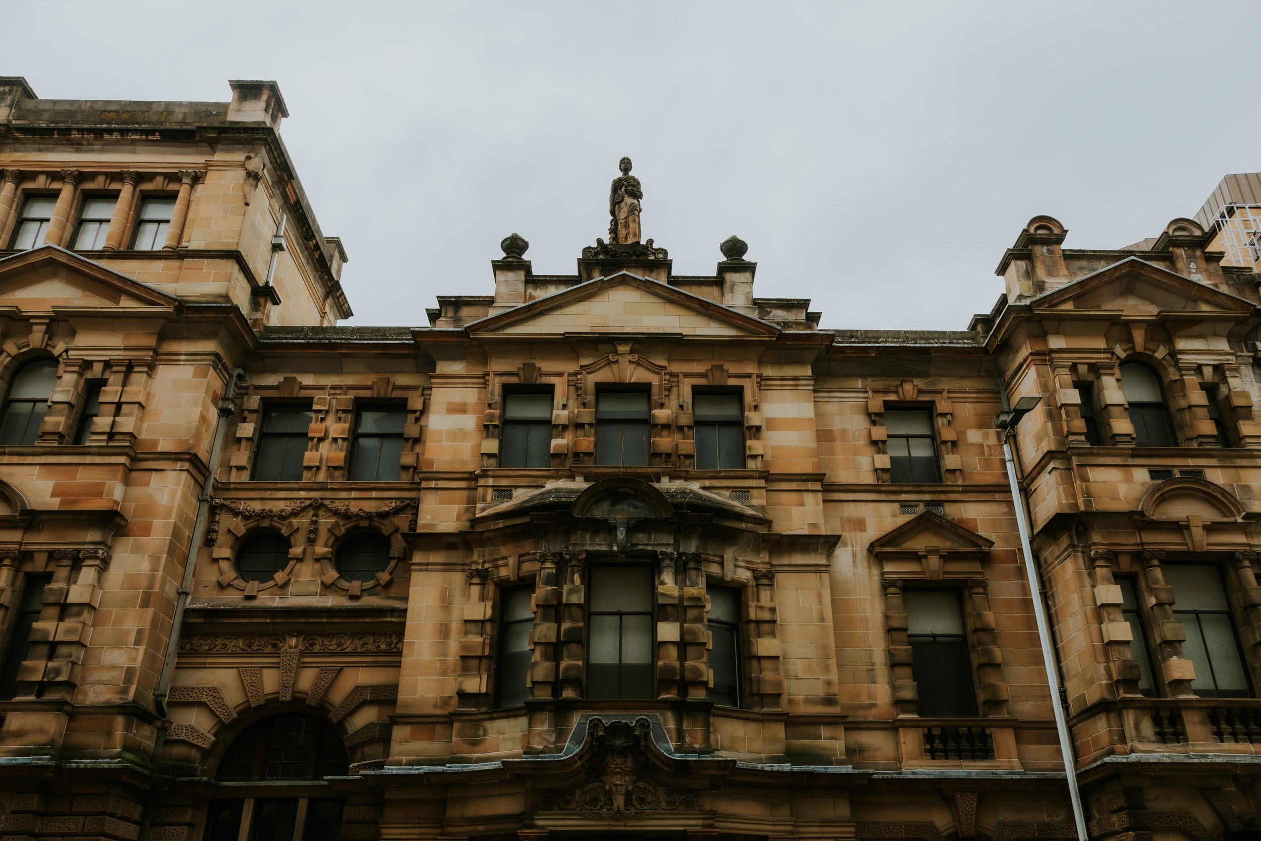 Alana & Kyle’s Glasgow Wedding — City Centre to The Bothy 1 Sandstone façade of Glasgow City Chambers with central statue on the pediment under a grey sky.