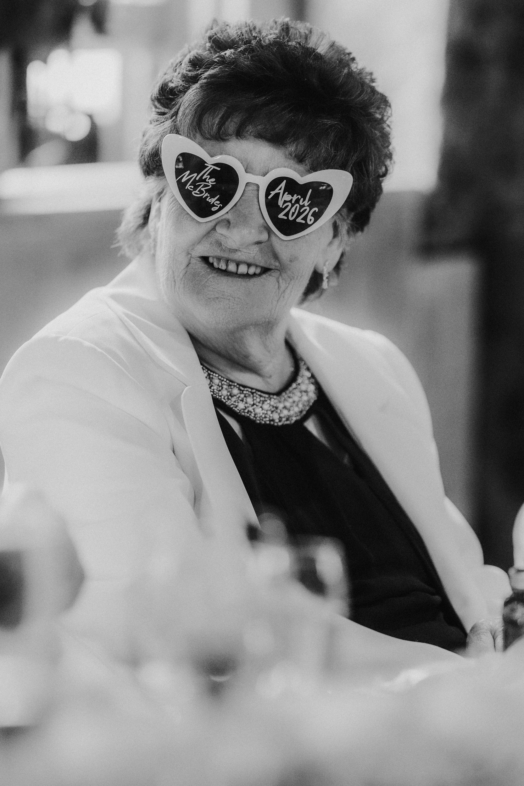 Alana & Kyle’s Glasgow Wedding — City Centre to The Bothy 25 Smiling older wedding guest wearing heart-shaped sunglasses reading 'The McBrides' and 'April 2026'.