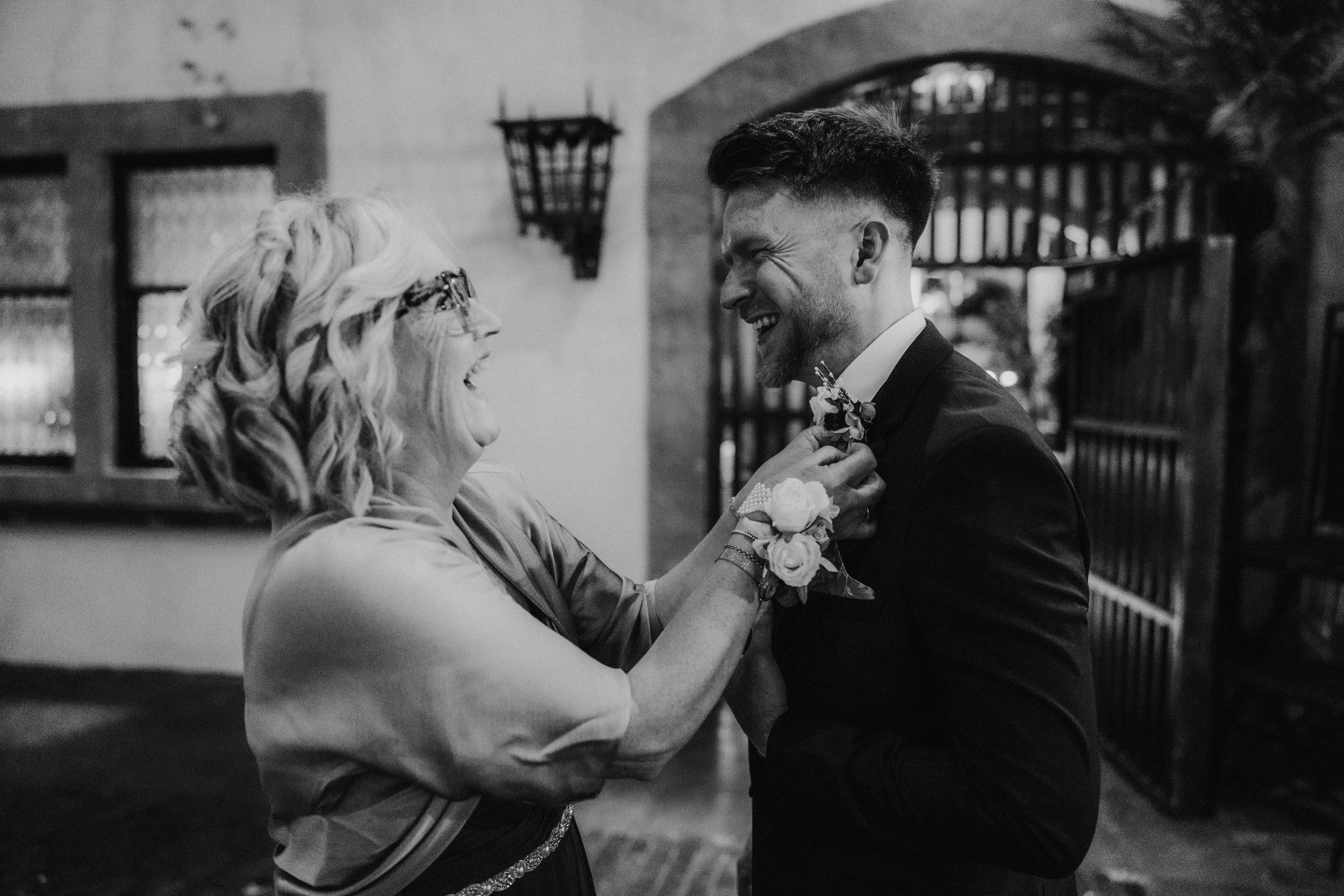 A woman adjusts John's floral buttonhole as they smile at each other at Arta, Glasgow.