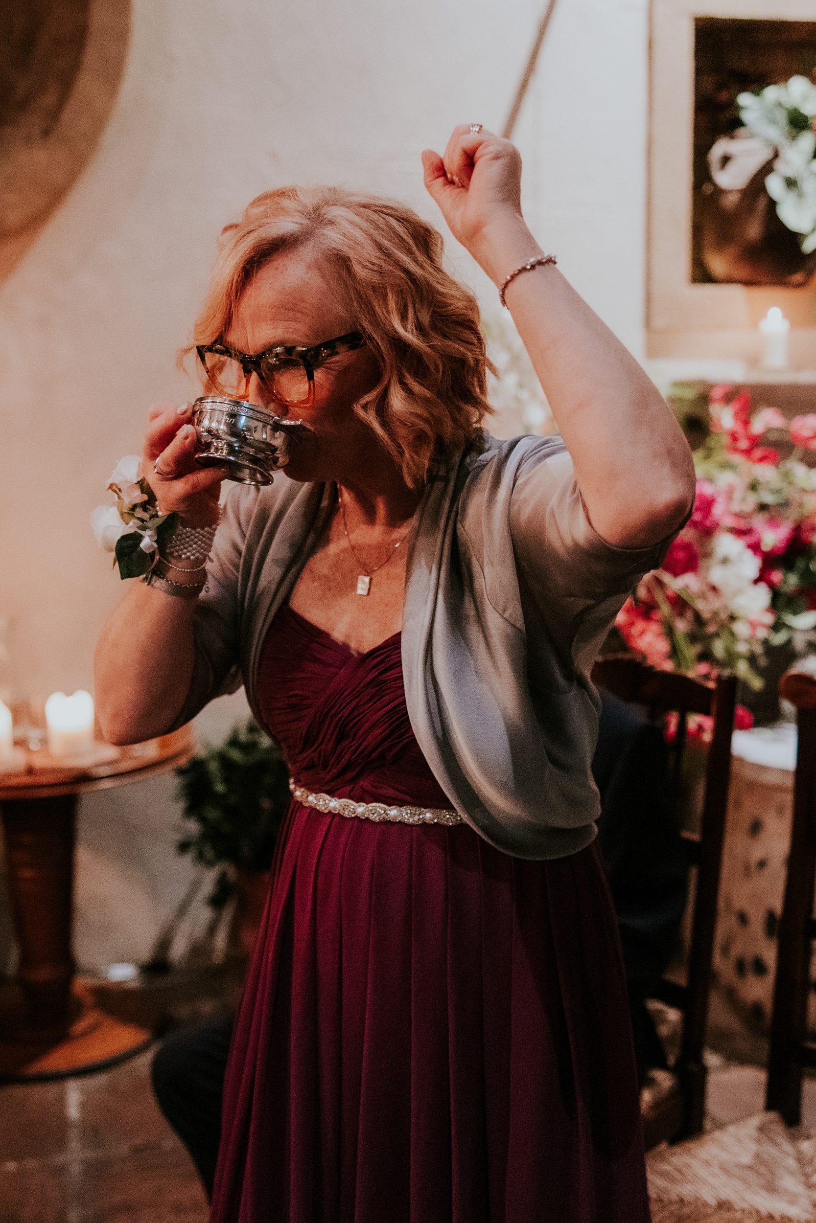 A woman in a burgundy dress drinks from a silver quaich with her other arm raised at Arta, Glasgow.