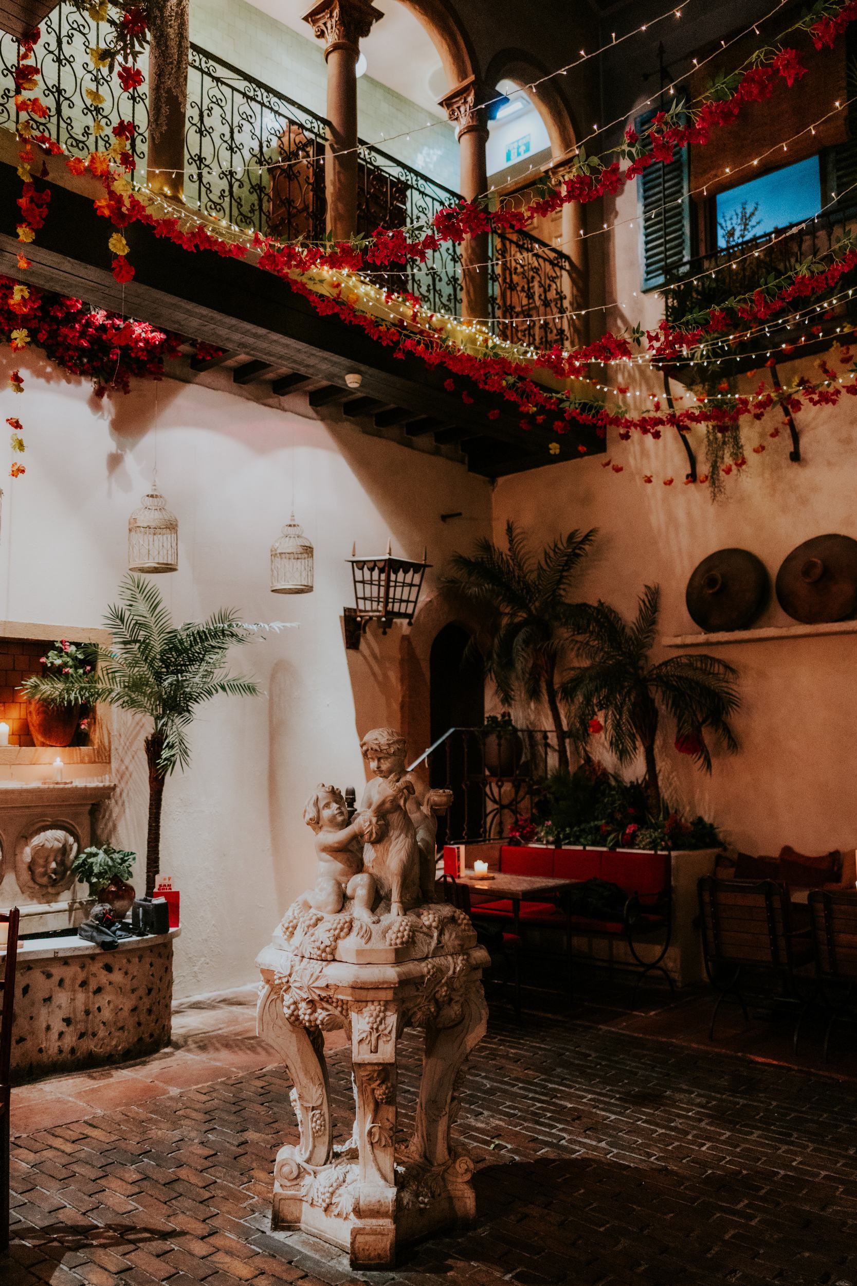 Arta in Glasgow with a central stone sculpture, palms, ornate balconies and floral garlands beneath fairy lights.