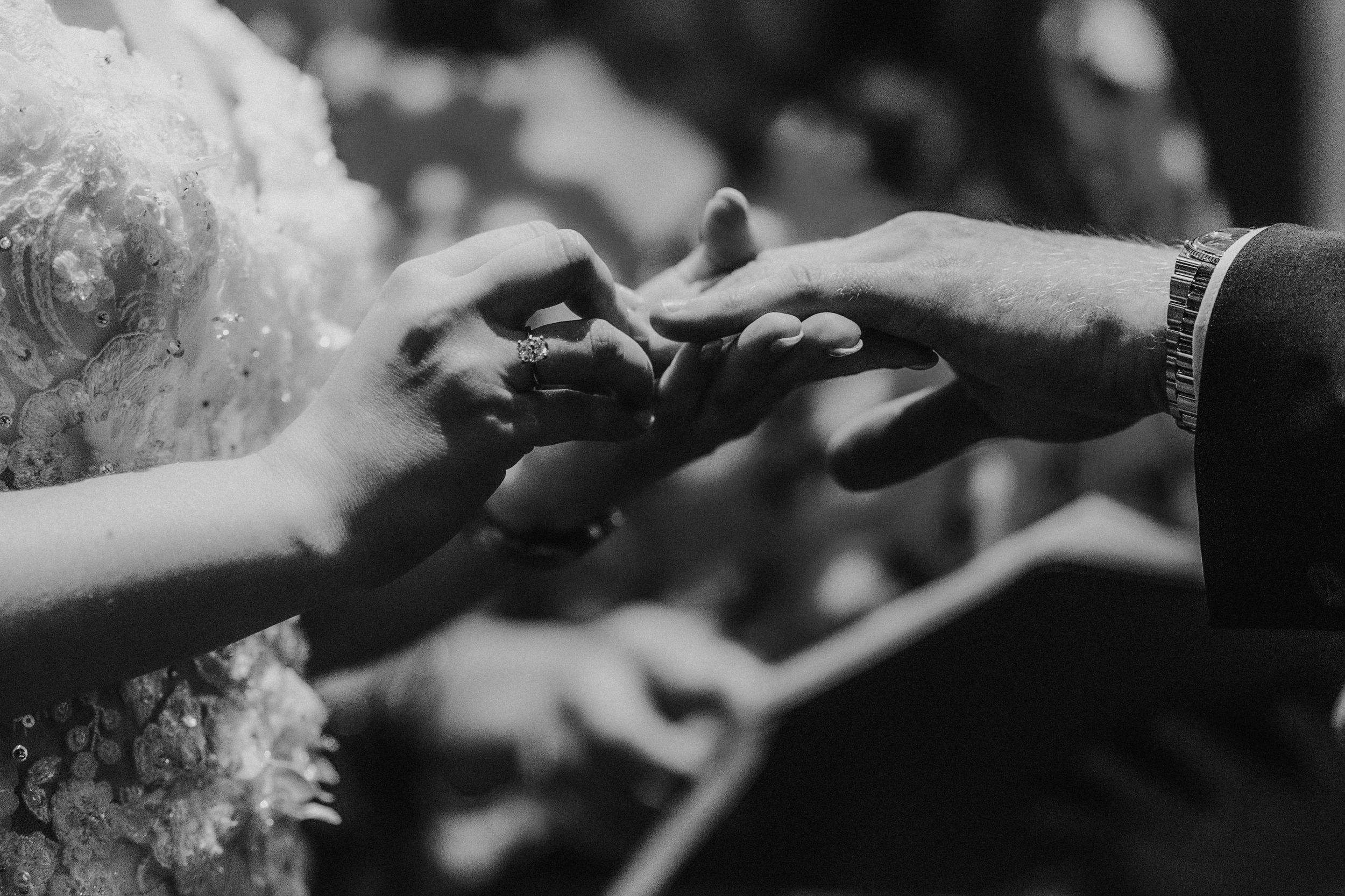 Black-and-white close-up of Lucy placing a wedding ring on John's finger at Arta, Glasgow.