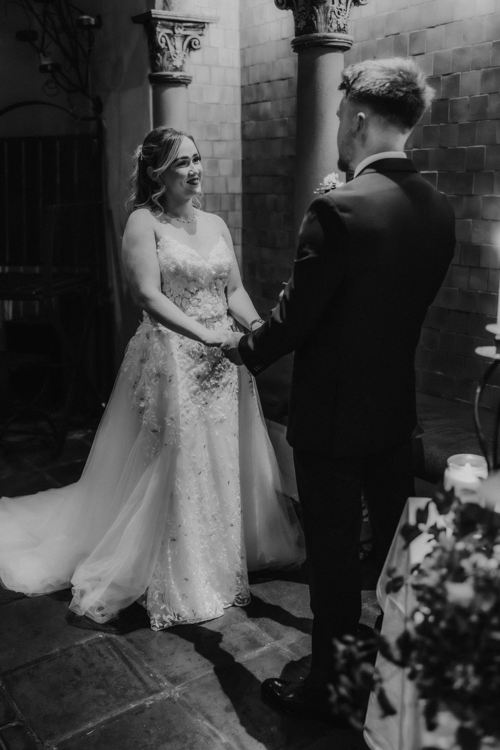 Black-and-white portrait of Lucy and John holding hands beside decorative columns and candles at Arta, Glasgow.