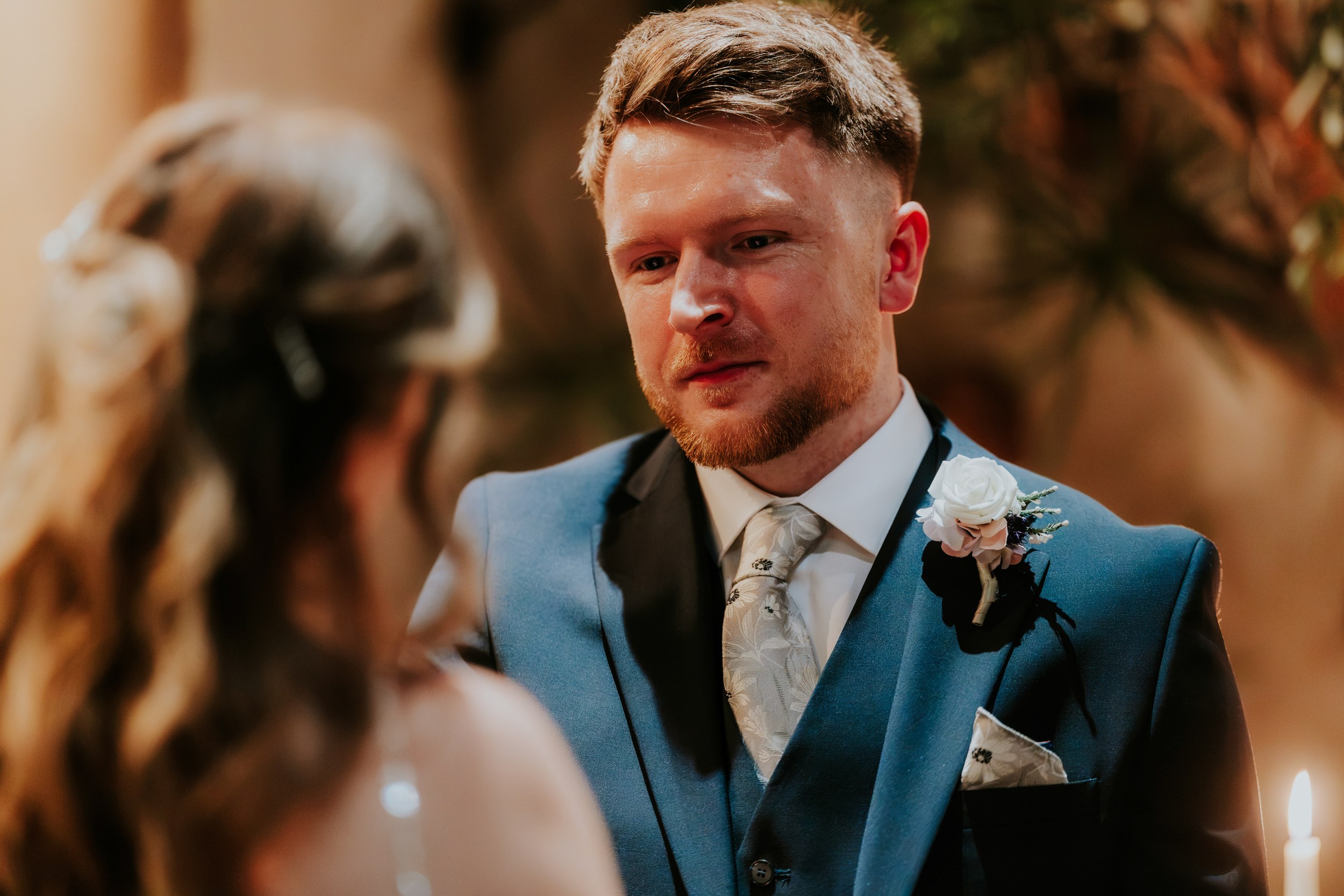 Close-up of John in a blue suit and white rose buttonhole, looking towards Lucy at Arta, Glasgow.