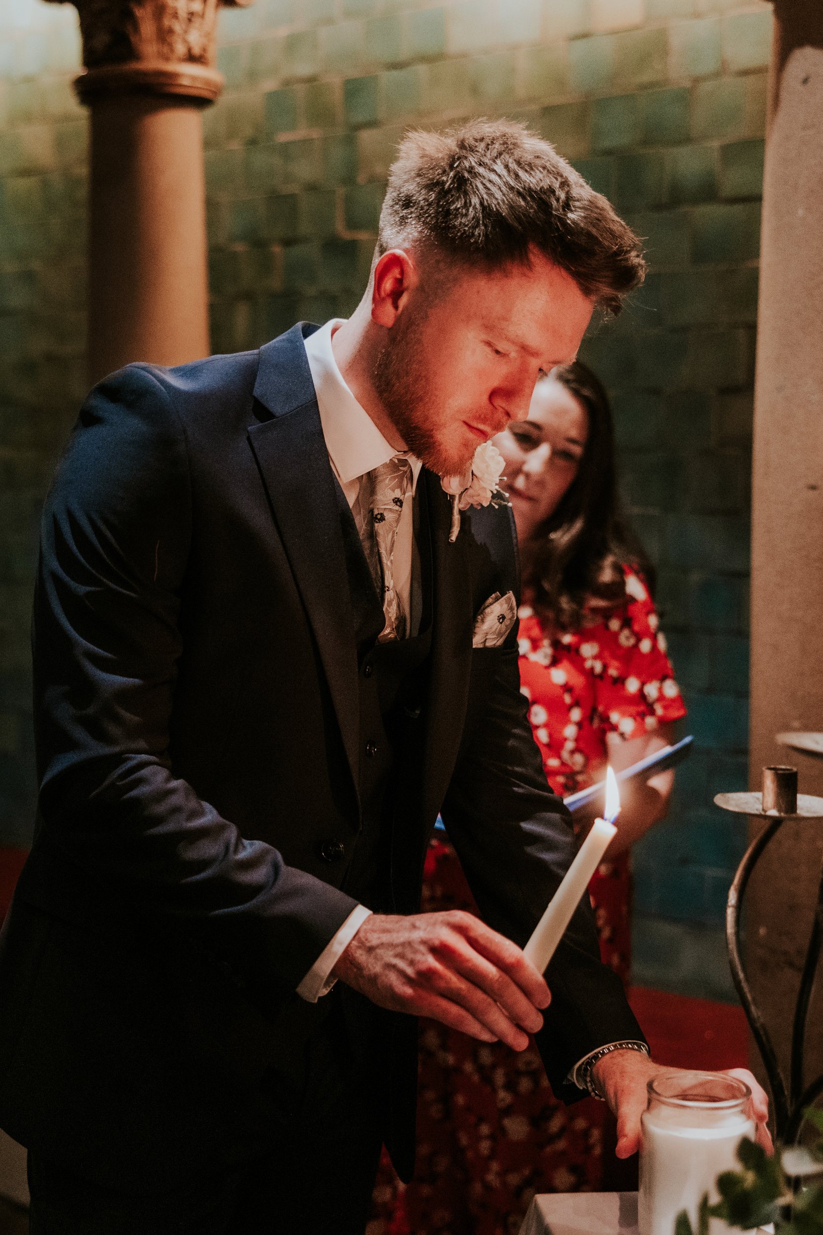 John holding a lit taper beside a glass candle jar during the wedding ceremony at Arta, Glasgow.