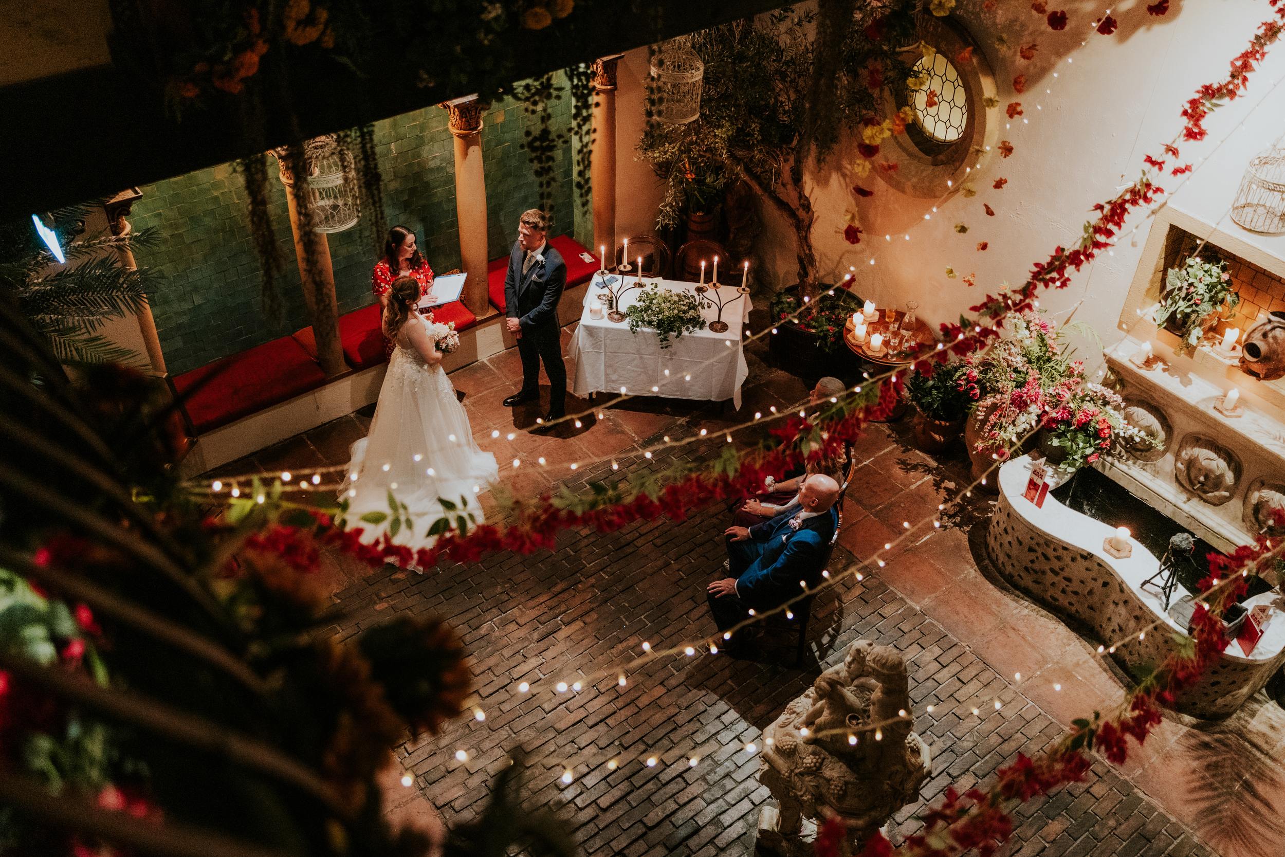 Lucy and John during their wedding ceremony at Arta, Glasgow, viewed from above through flowers and fairy lights.