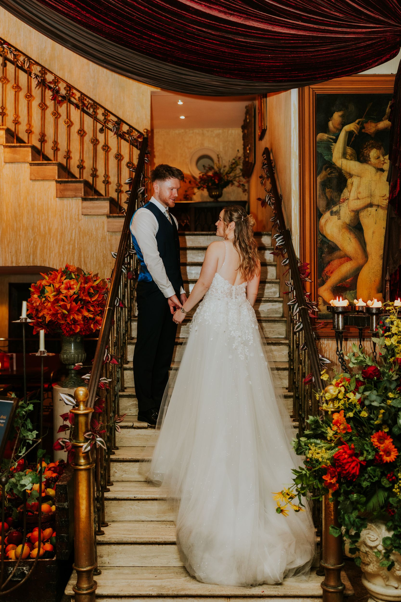 Lucy and John holding hands on the ornate staircase at Arta, Glasgow, with flowers and candles beside them.
