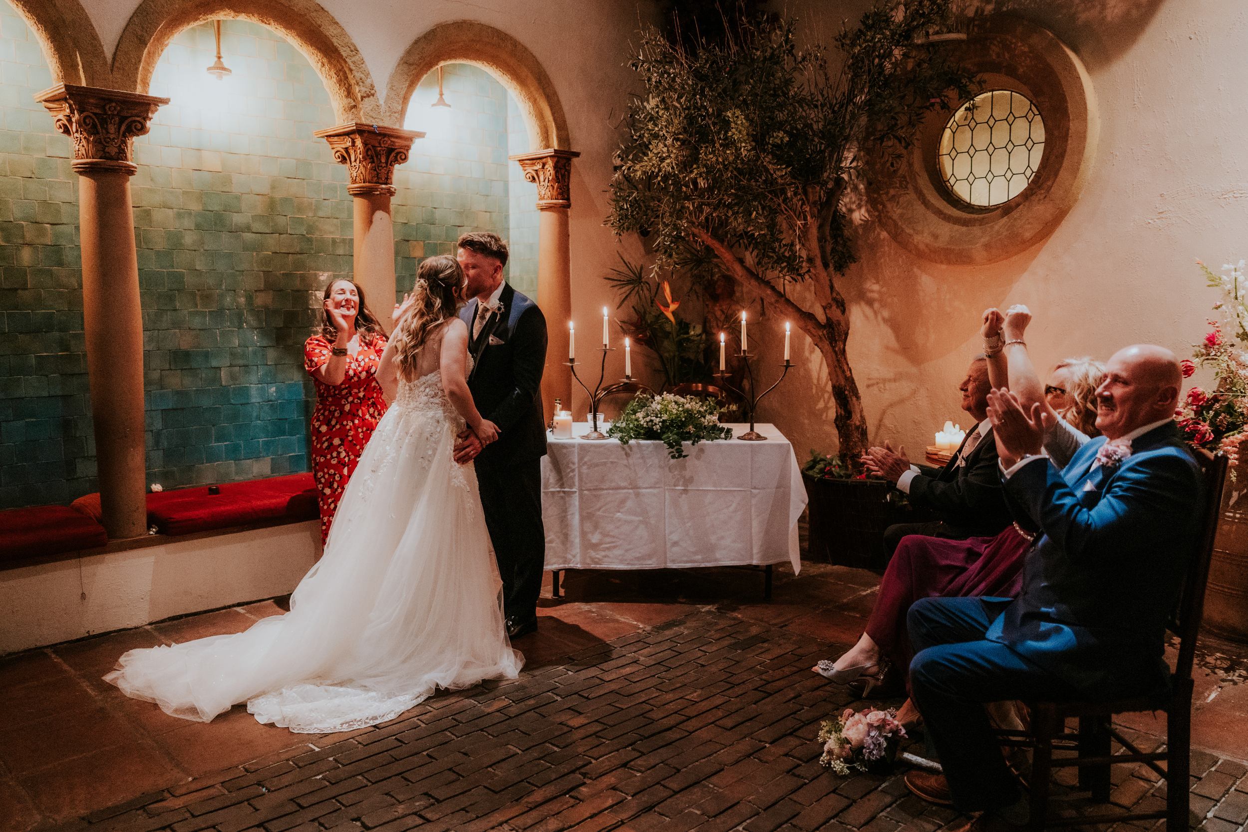 Lucy and John kiss during their wedding ceremony at Arta in Glasgow as guests applaud.