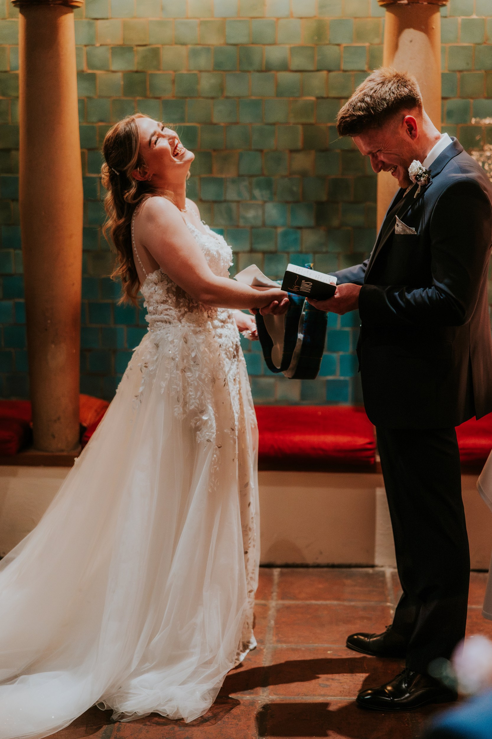 Lucy and John laughing during their handfasting ceremony at Arta, Glasgow, with John holding his vow booklet.