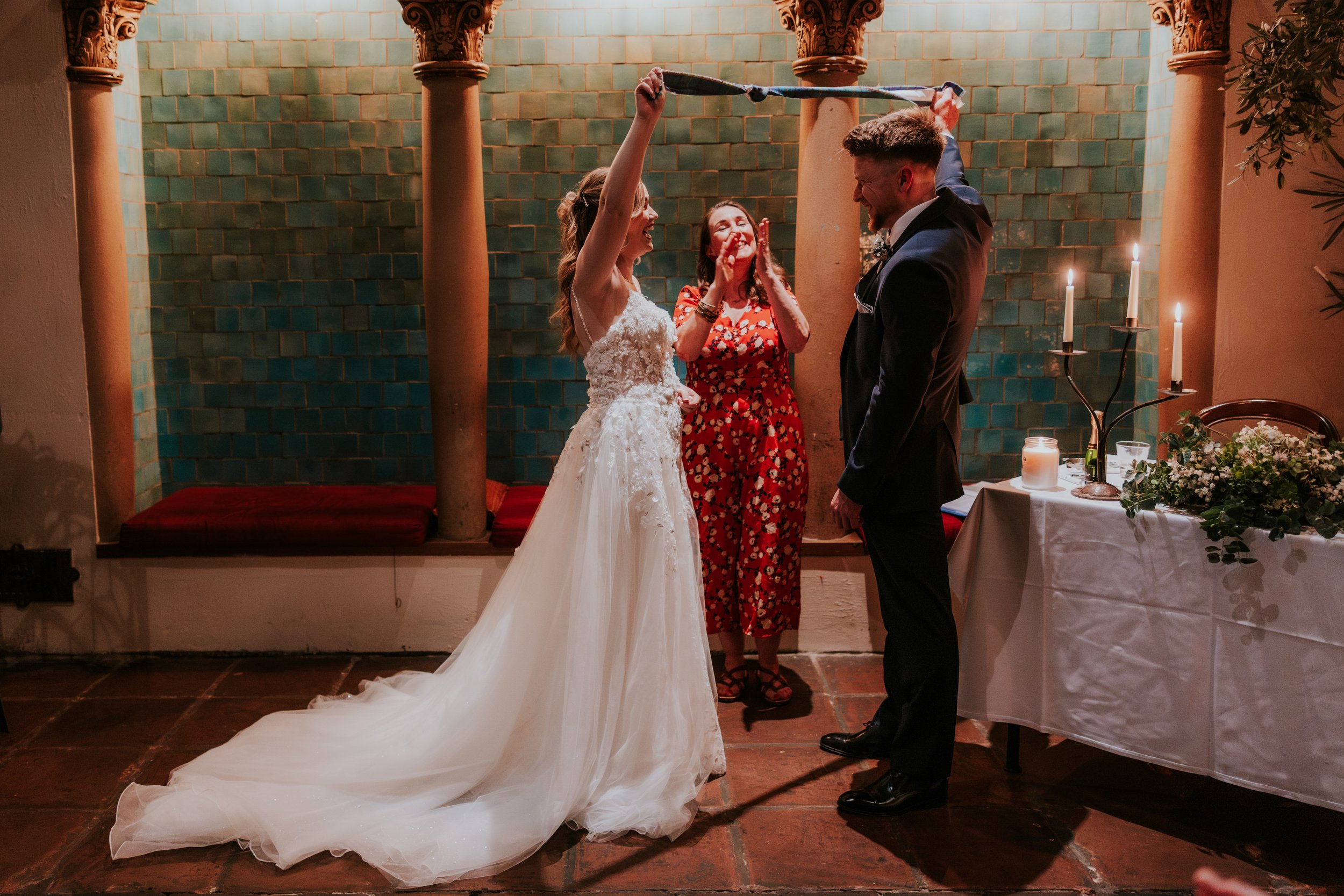 Lucy and John raise their tartan handfasting ribbon as the celebrant applauds during their ceremony at Arta, Glasgow.