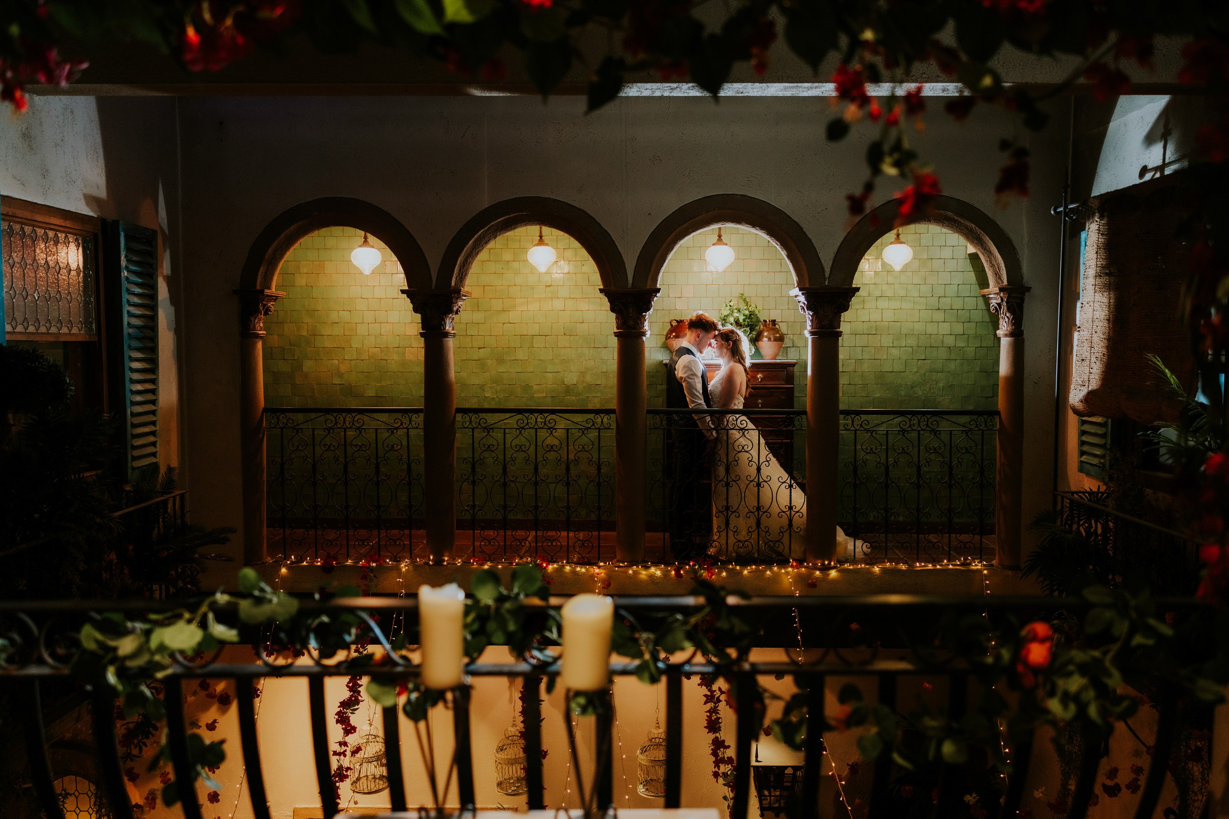 Lucy and John standing face to face beneath stone arches on Arta’s indoor balcony in Glasgow.