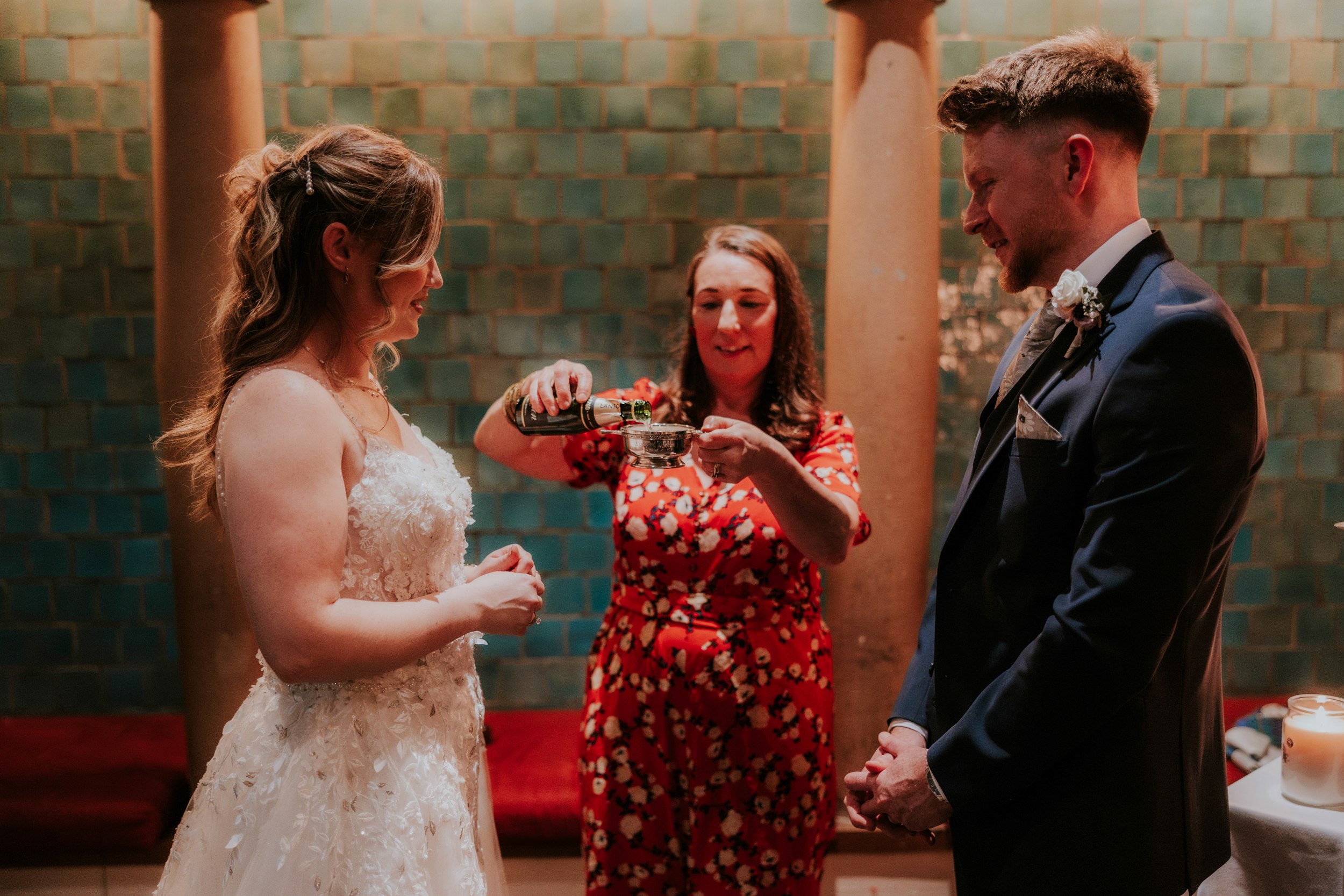 Lucy and John watch champagne being poured into a silver quaich during their wedding ceremony at Arta, Glasgow.