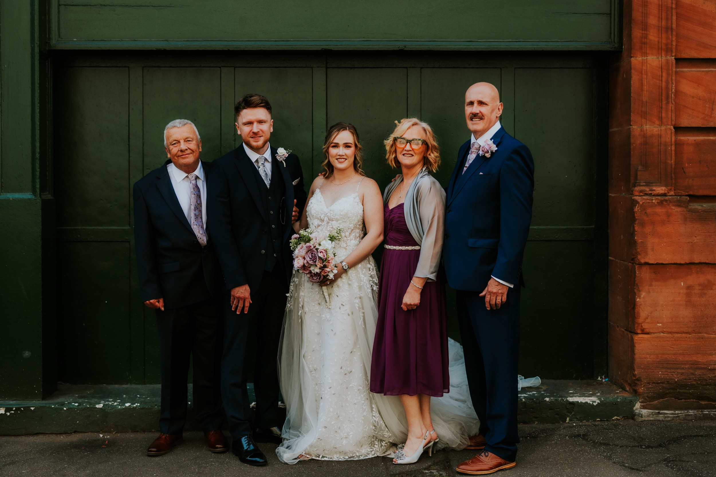 Lucy and John with three wedding guests in front of dark green doors and red sandstone in Glasgow.