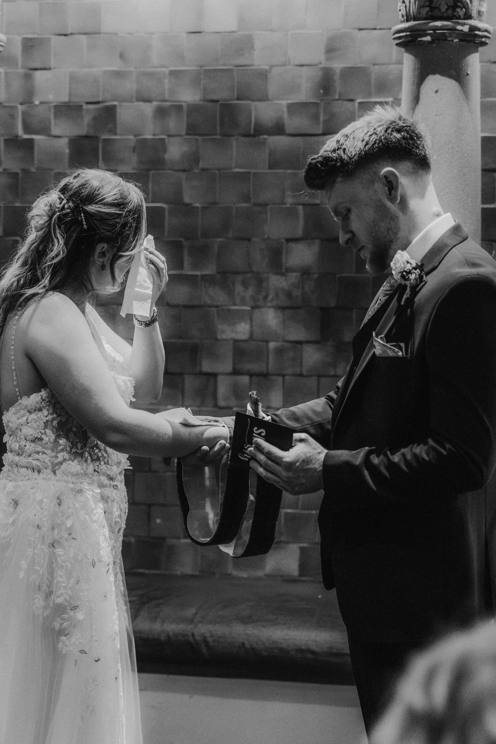 Lucy dabs her eye as John holds his vows, their hands joined with handfasting ribbons during their ceremony at Arta, Glasgow.