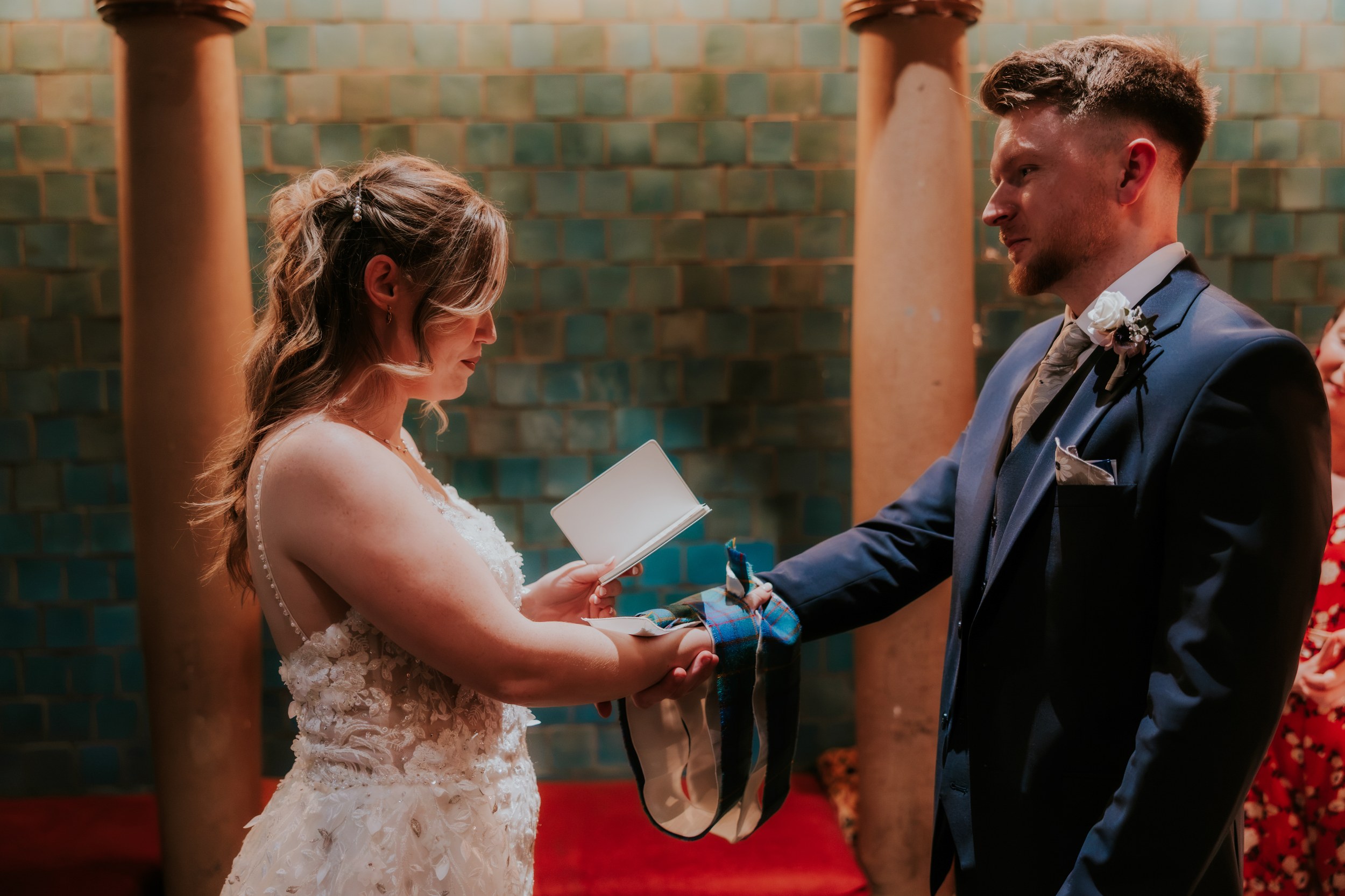 Lucy reads from a booklet as she and John hold hands wrapped in tartan during their handfasting at Arta, Glasgow.