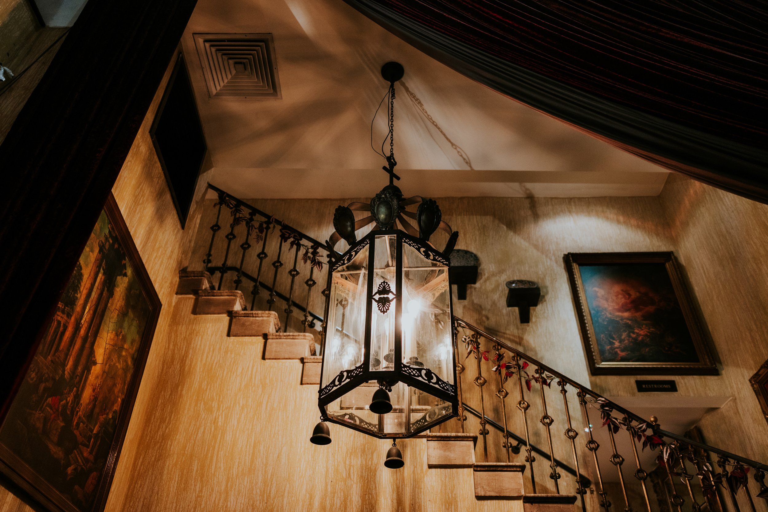 Ornate hanging lantern beside a stone staircase with decorative metal railings and dark red drapes at Arta, Glasgow.