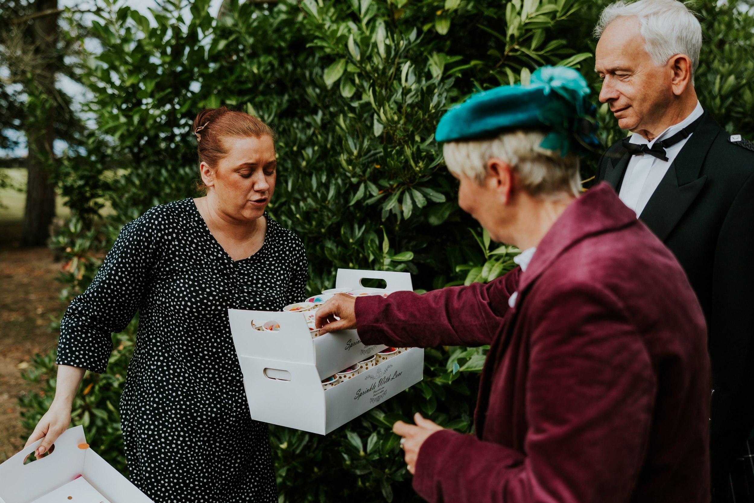 A guest in a teal hat collects a cup of colourful confetti from a tray outdoors at Lochgreen House Hotel.