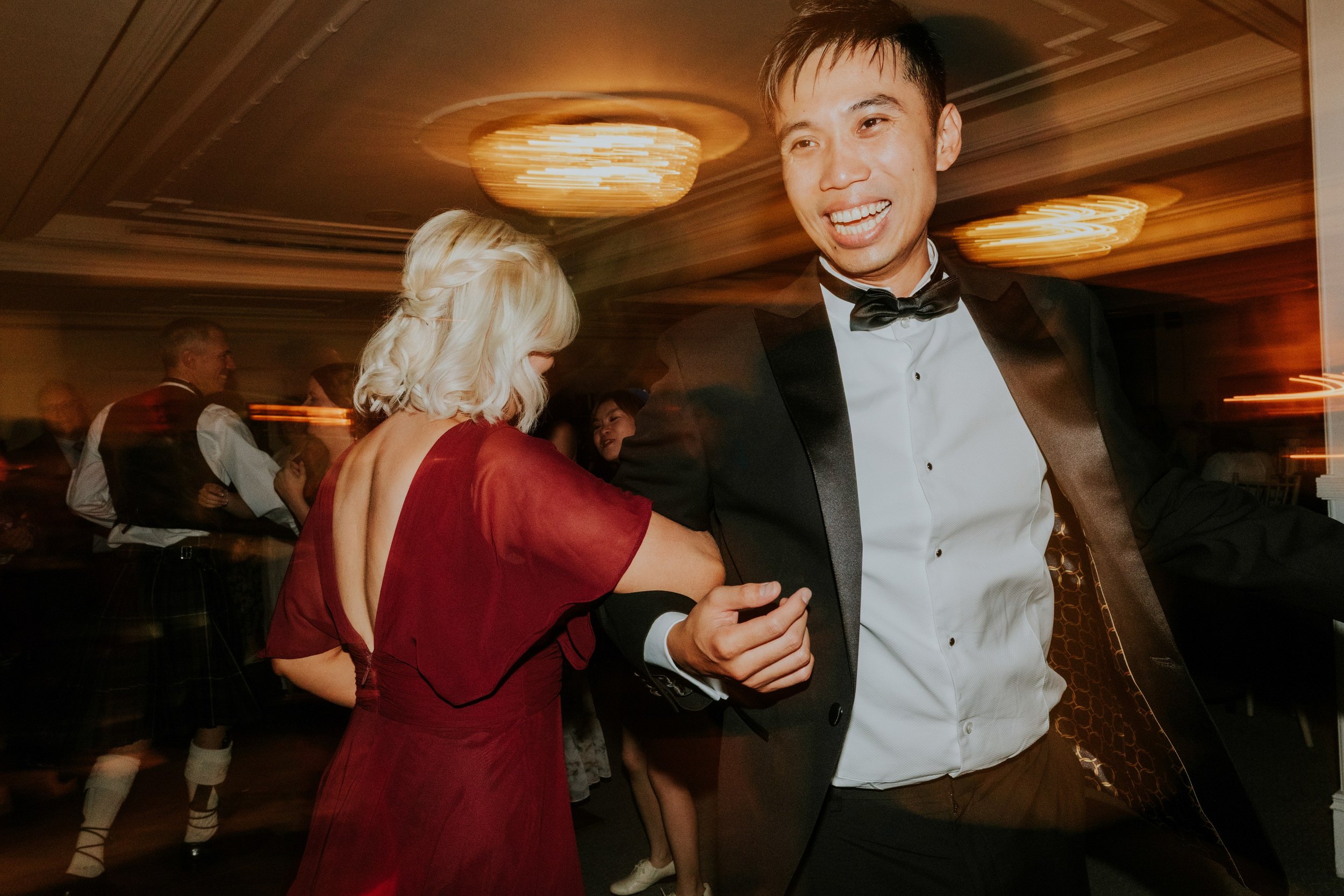 A man in a black dinner suit and a woman in a burgundy dress dancing at Lochgreen House Hotel.