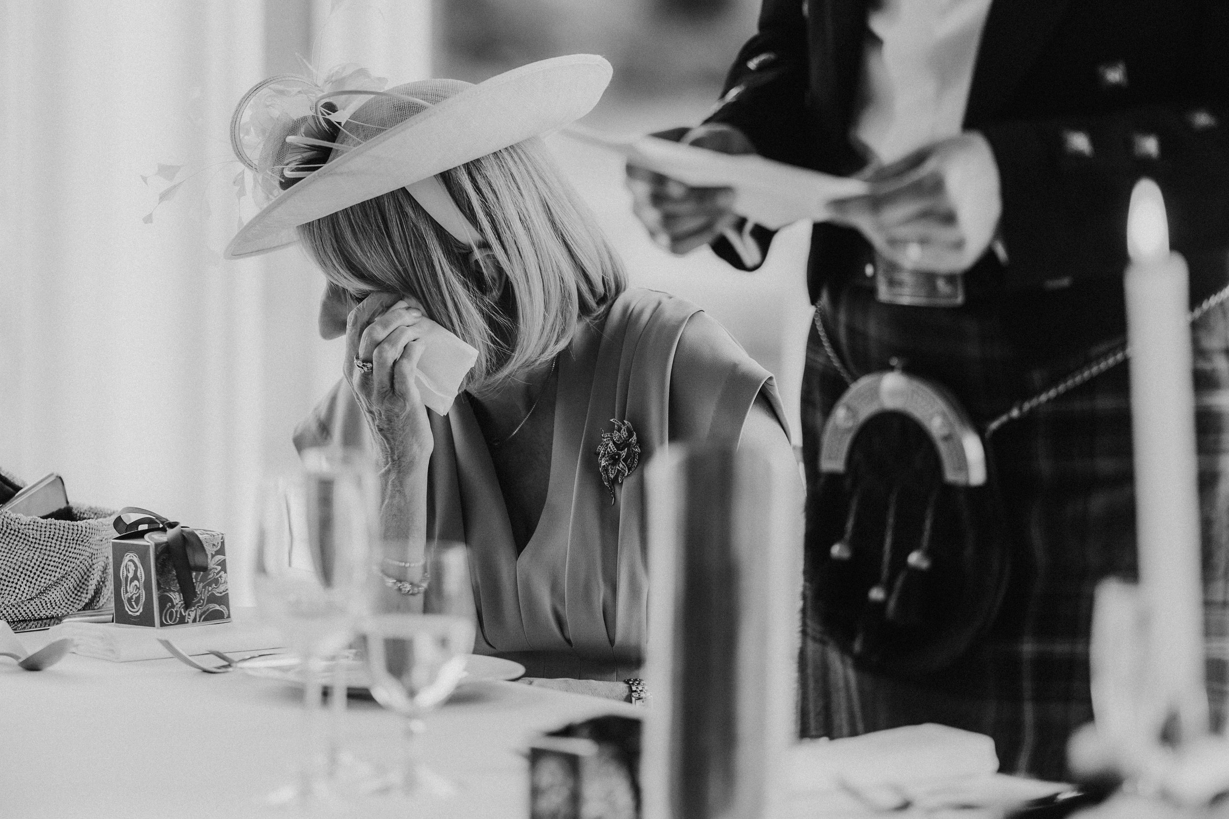 A woman dabs her eye with a tissue as a man in Highland dress holds speech notes behind her at Lochgreen House Hotel.