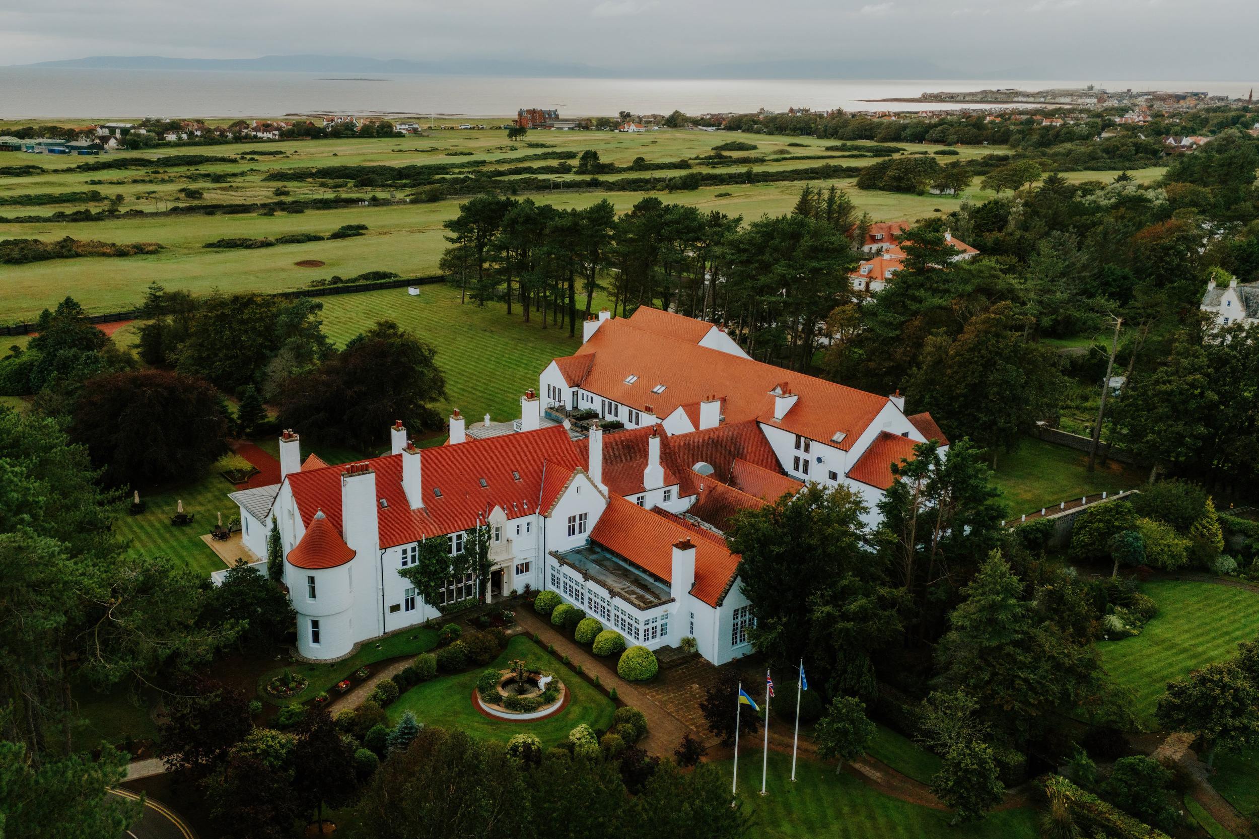 Aerial view of Lochgreen House Hotel and its gardens, with a golf course and the sea beyond.