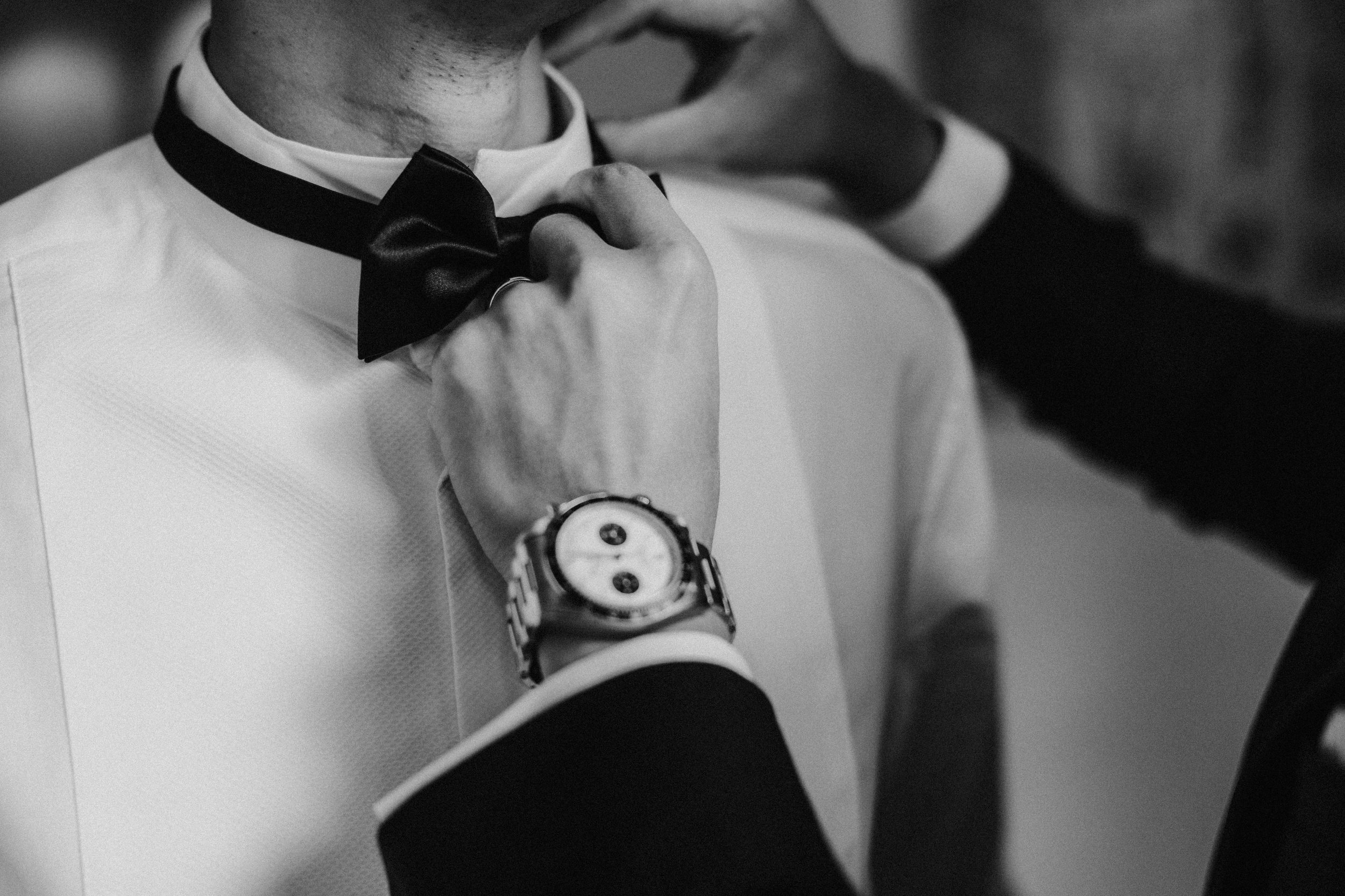 Black-and-white close-up of hands adjusting a black bow tie on a man's white dress shirt.