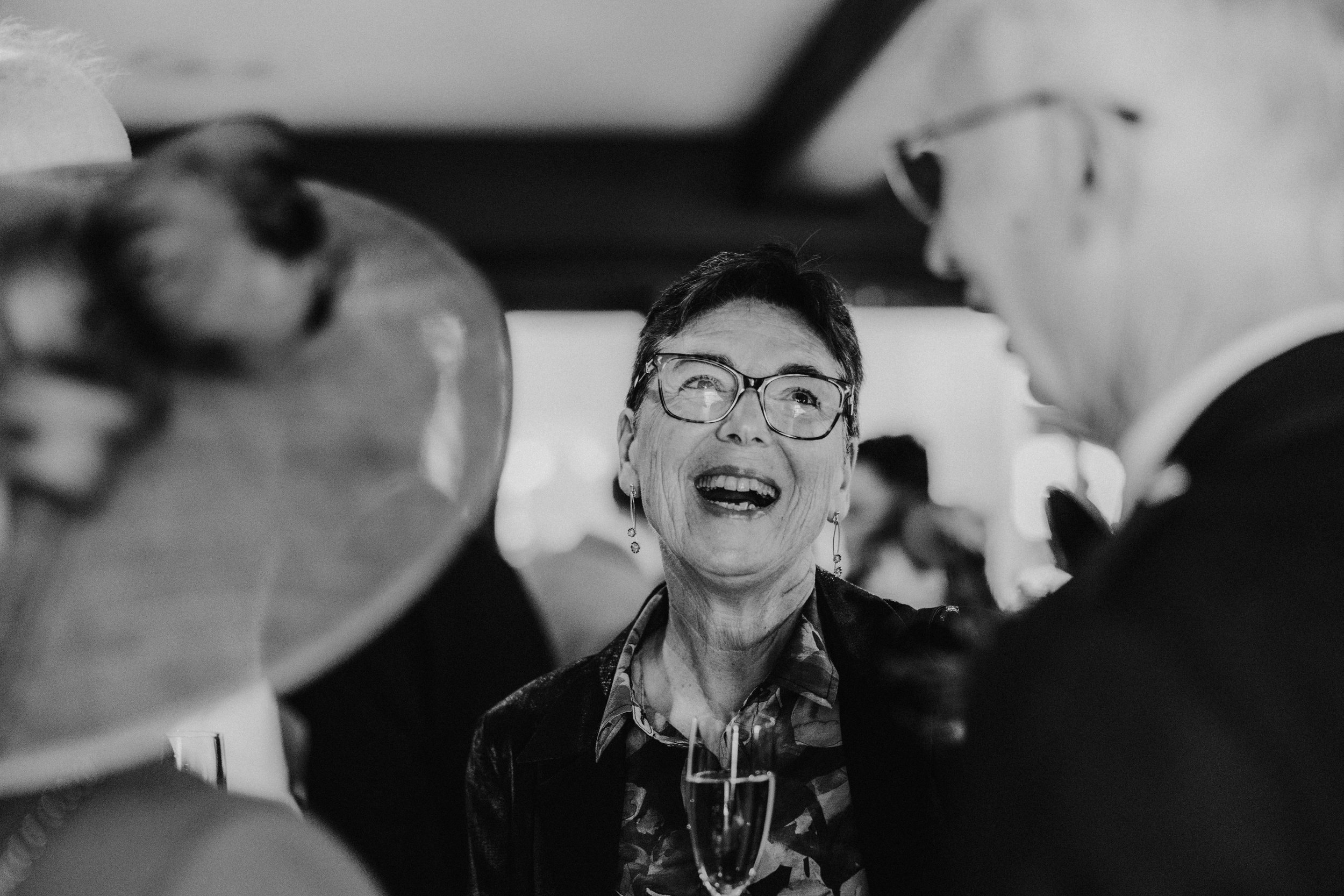 Black-and-white photograph of a wedding guest laughing among guests with a champagne flute at Lochgreen House Hotel.