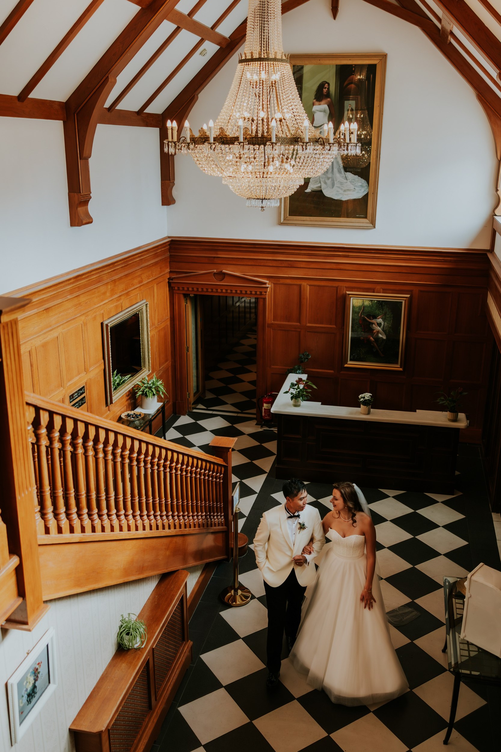 Emma and Gordon arm in arm beneath a chandelier in Lochgreen House Hotel's wood-panelled hall.