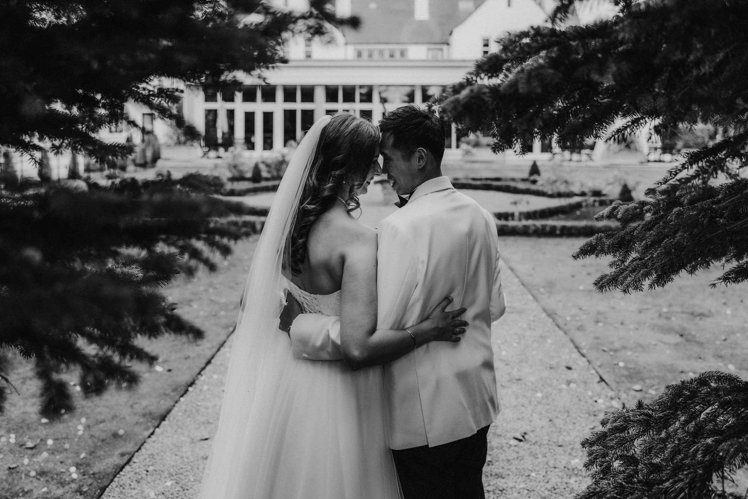 Emma and Gordon embracing beneath tree branches outside Lochgreen House Hotel in a black-and-white portrait.
