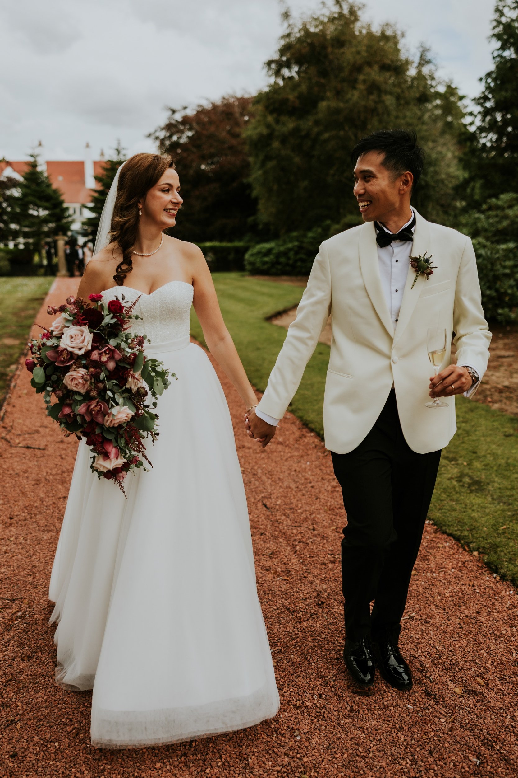 Emma and Gordon holding hands and smiling at each other on a garden path at Lochgreen House Hotel.