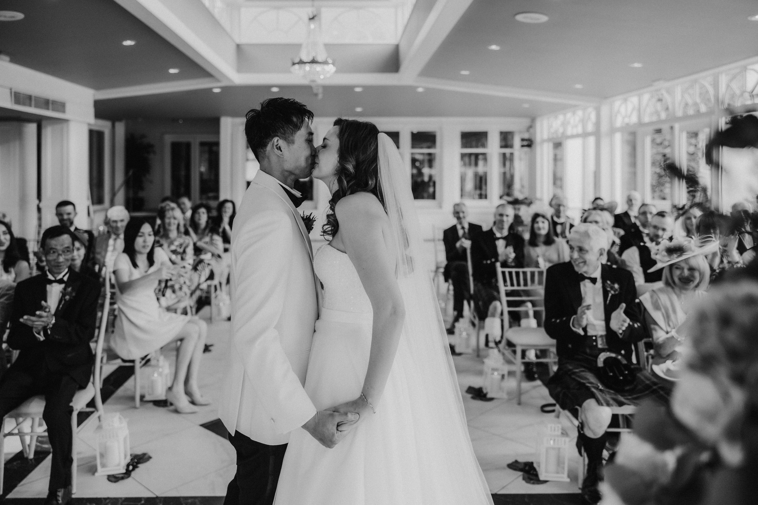 Emma and Gordon kiss as guests applaud during their ceremony in the orangery at Lochgreen House Hotel.