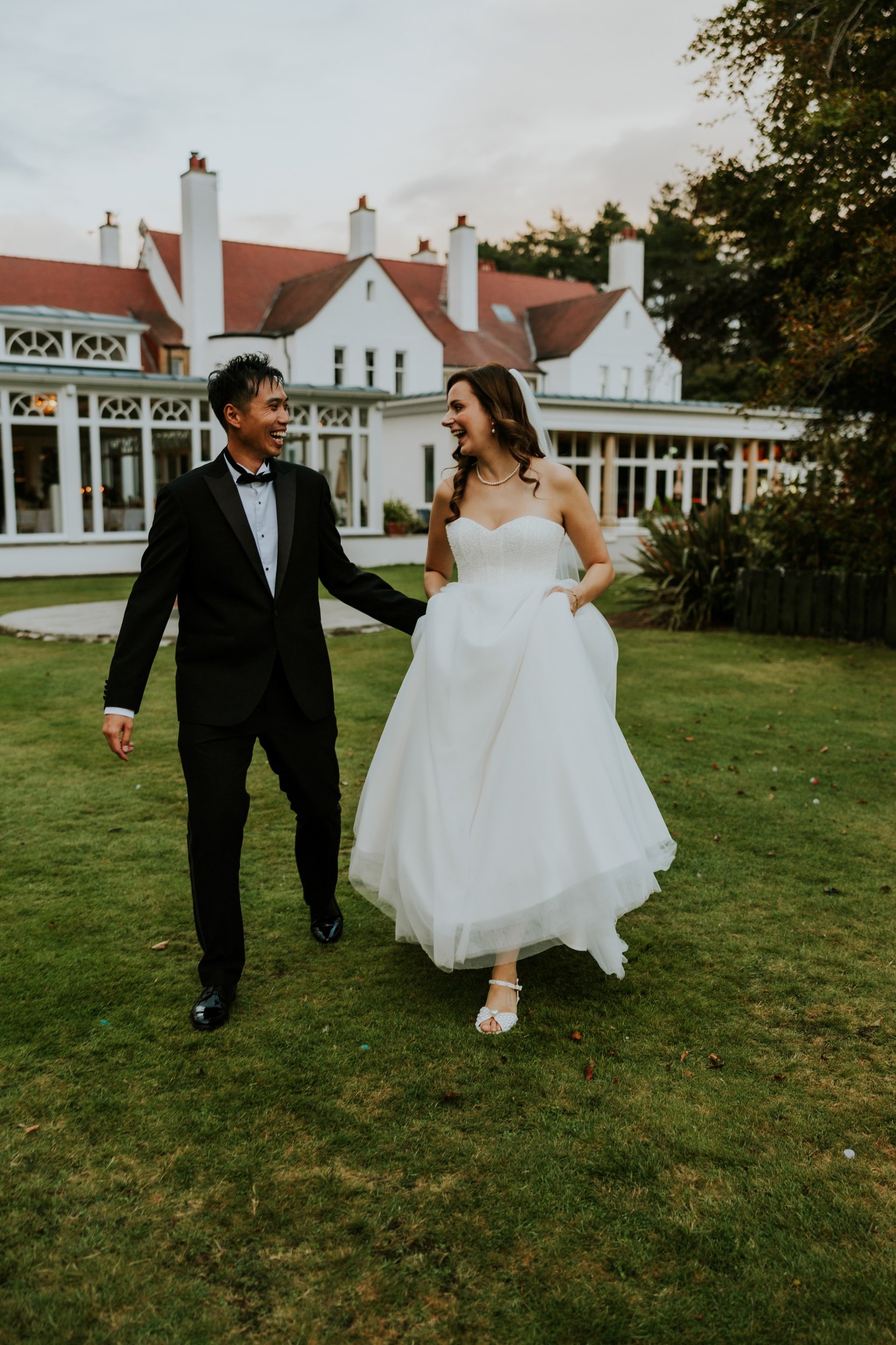 Emma and Gordon laughing as they walk across the lawn in front of Lochgreen House Hotel.