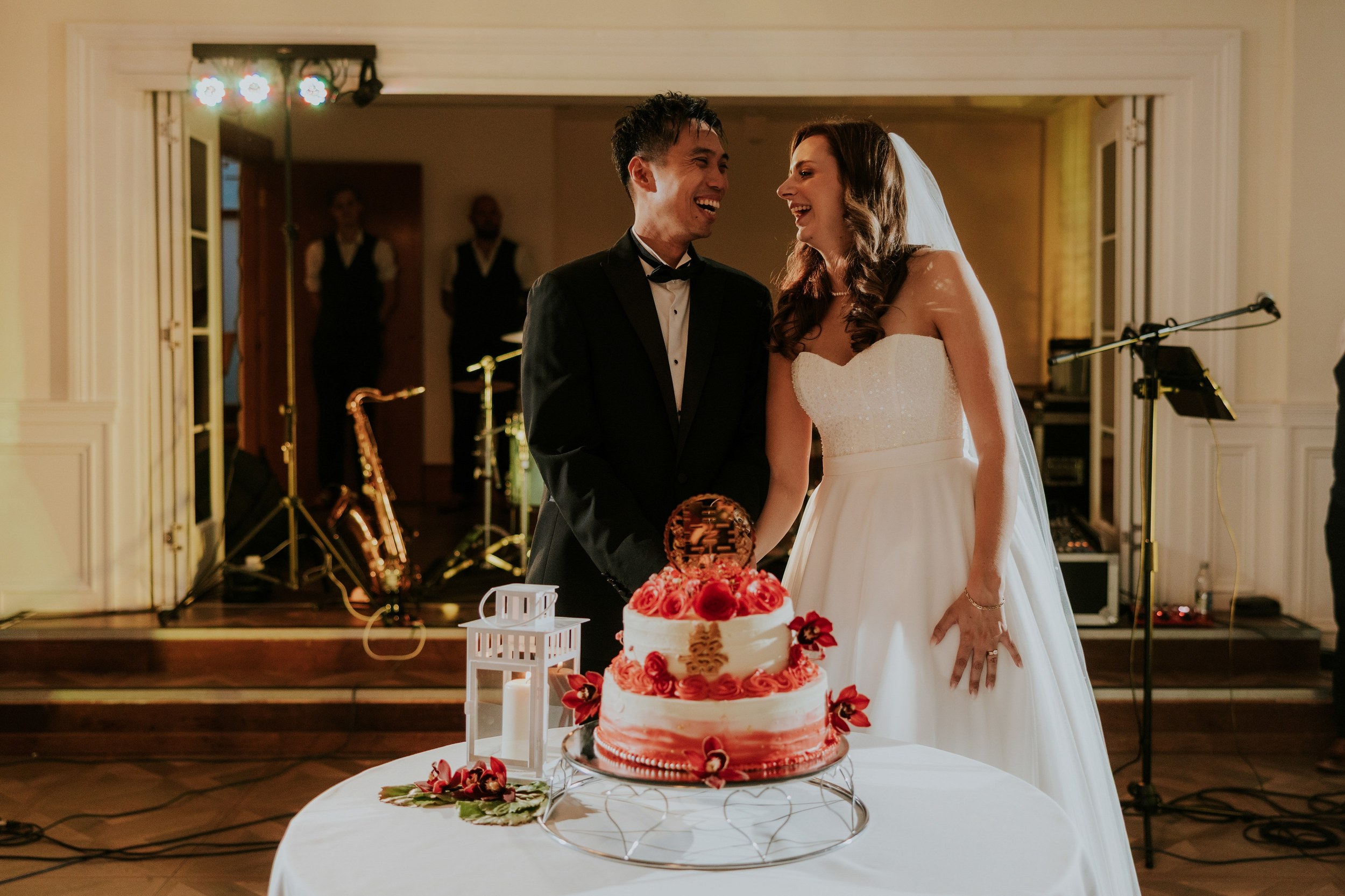 Emma and Gordon laughing together behind their red-and-white wedding cake at Lochgreen House Hotel.
