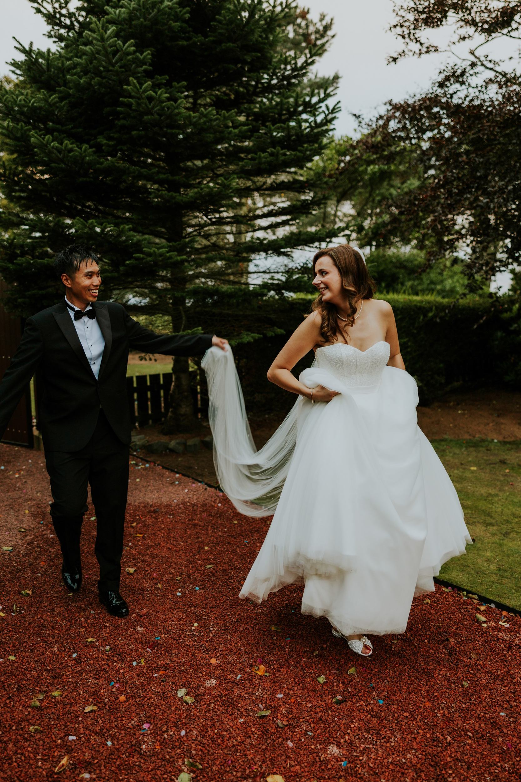 Emma and Gordon smiling on a garden path at Lochgreen House Hotel, with Gordon holding Emma's veil.