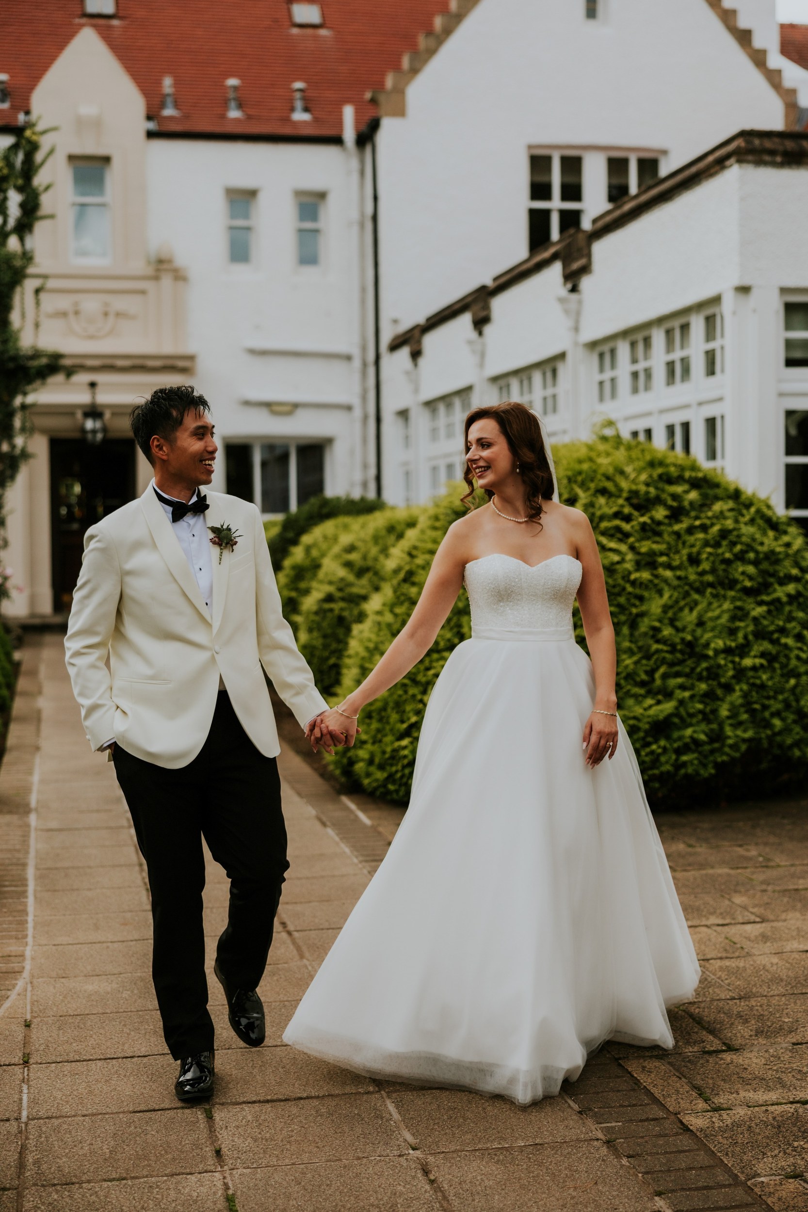 Emma and Gordon walking hand in hand and smiling at each other outside Lochgreen House Hotel.