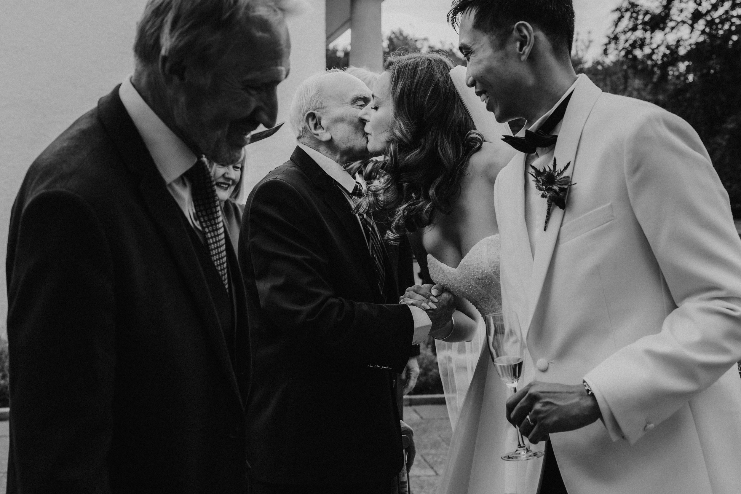 Emma greets a guest with a kiss as Gordon smiles beside her holding a champagne flute at Lochgreen House Hotel.