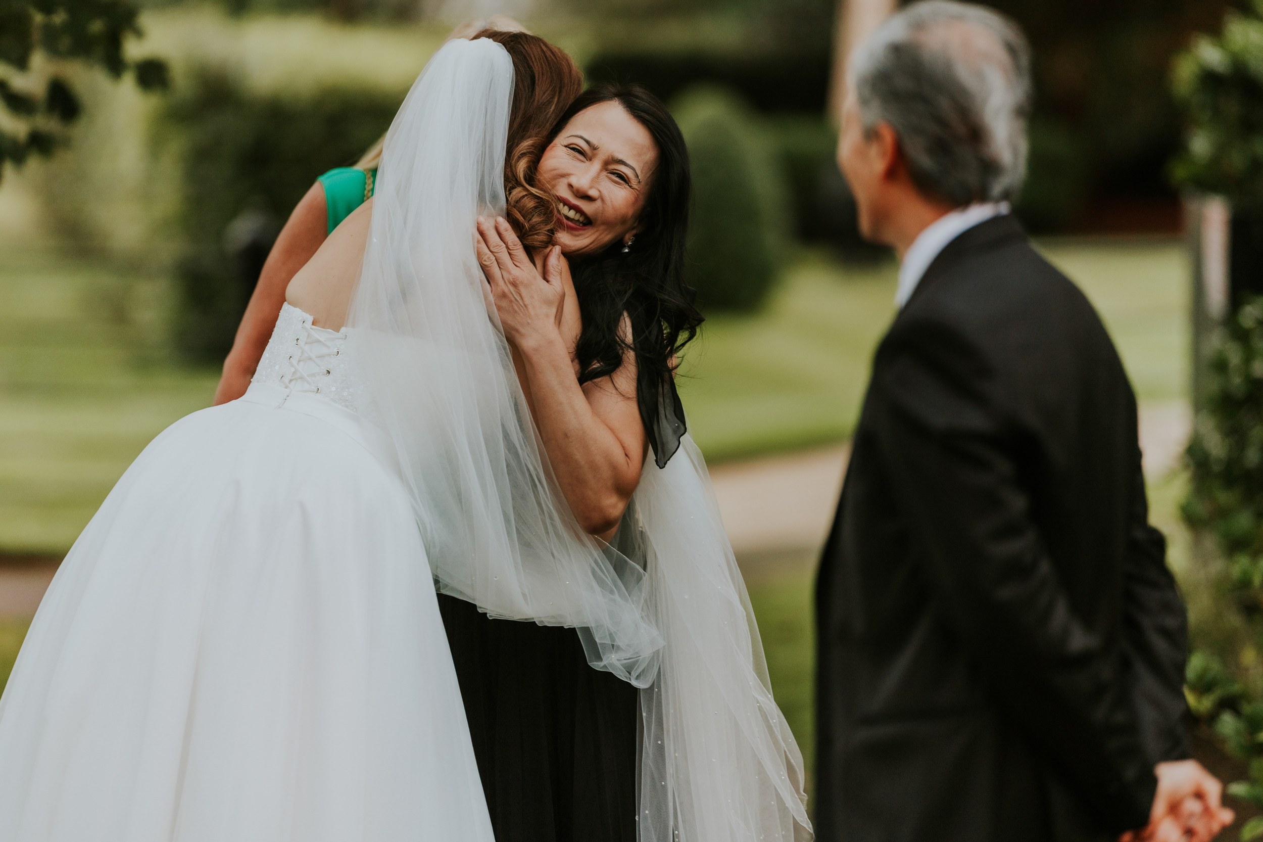 Emma hugs a smiling guest in the grounds of Lochgreen House Hotel while a man in a dark suit looks on.