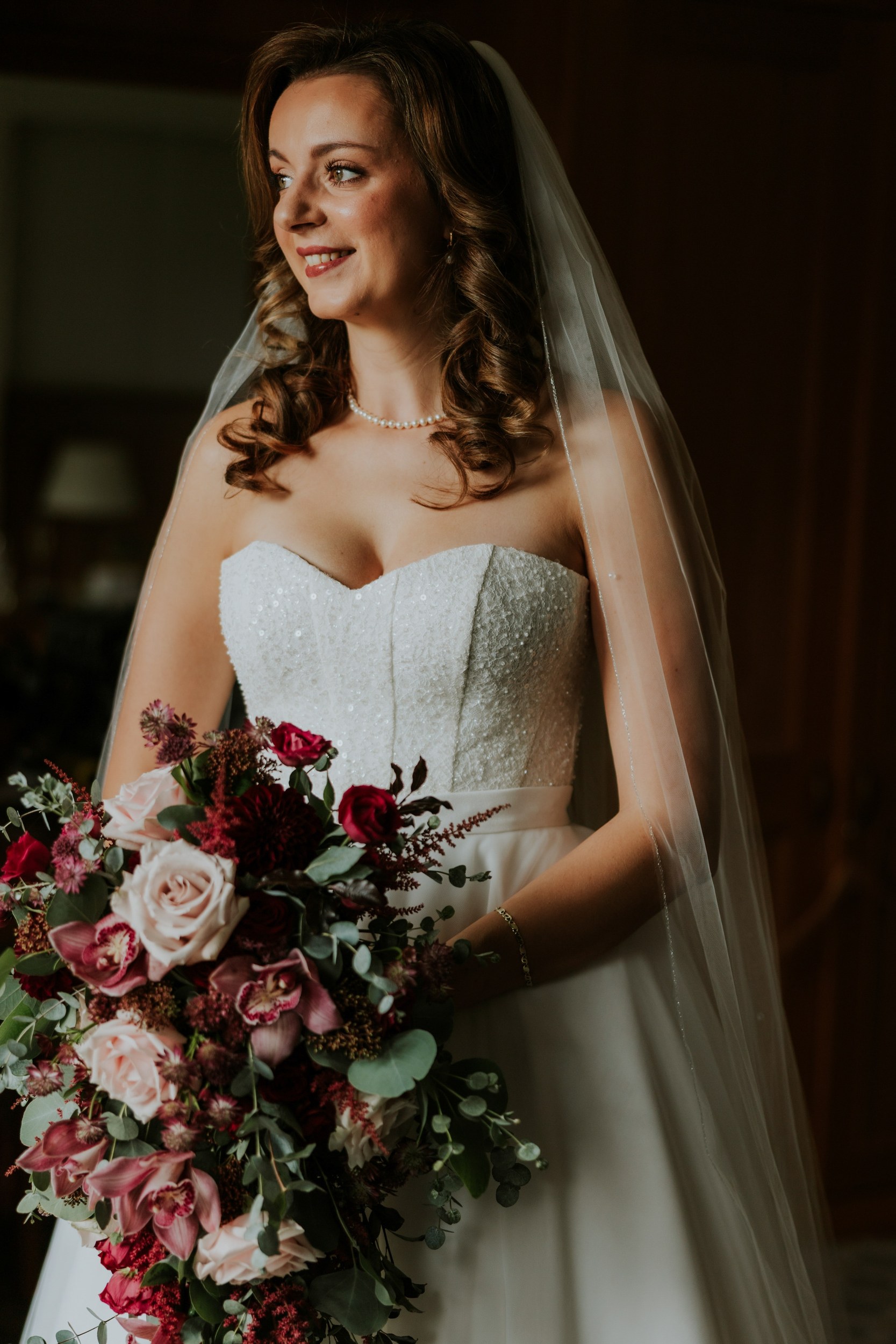 Emma in her wedding dress and veil, holding a cascading pink and burgundy bouquet at Lochgreen House Hotel.