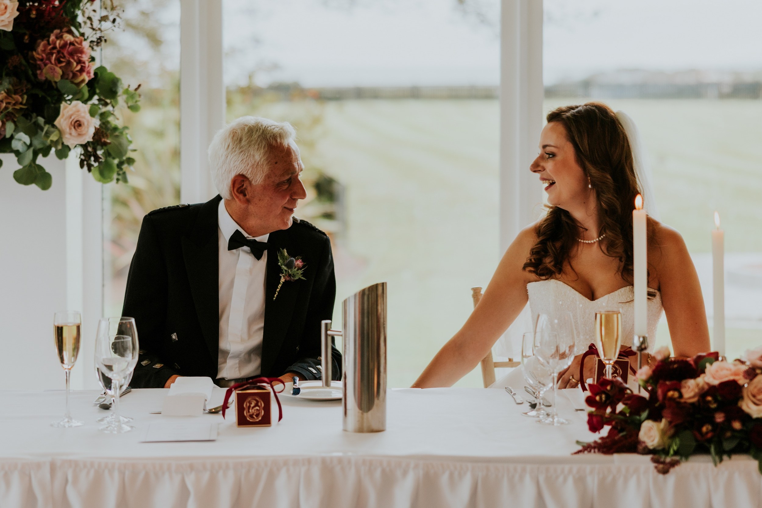 Emma smiling at a man beside her at a candlelit reception table at Lochgreen House Hotel.