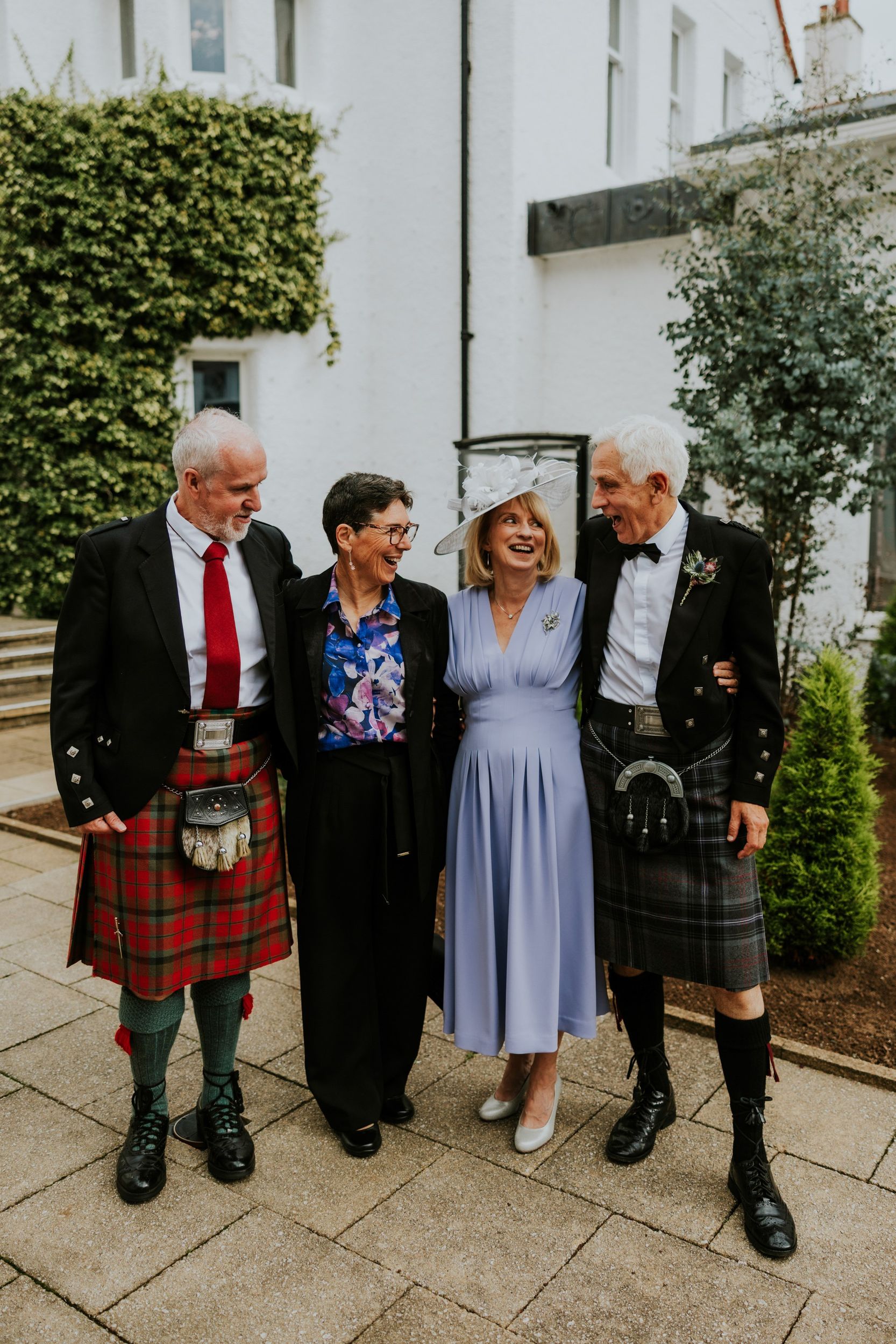 Four wedding guests laughing together during a group photograph outside Lochgreen House Hotel.