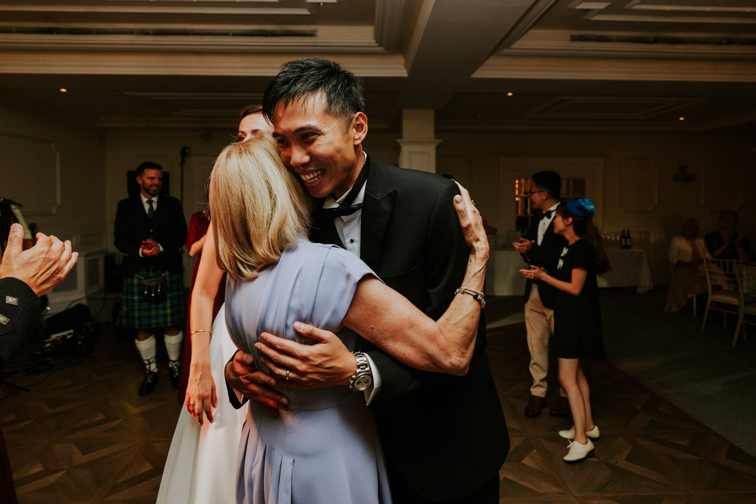 Gordon hugging a guest in a pale blue dress as others applaud on the dance floor at Lochgreen House Hotel.