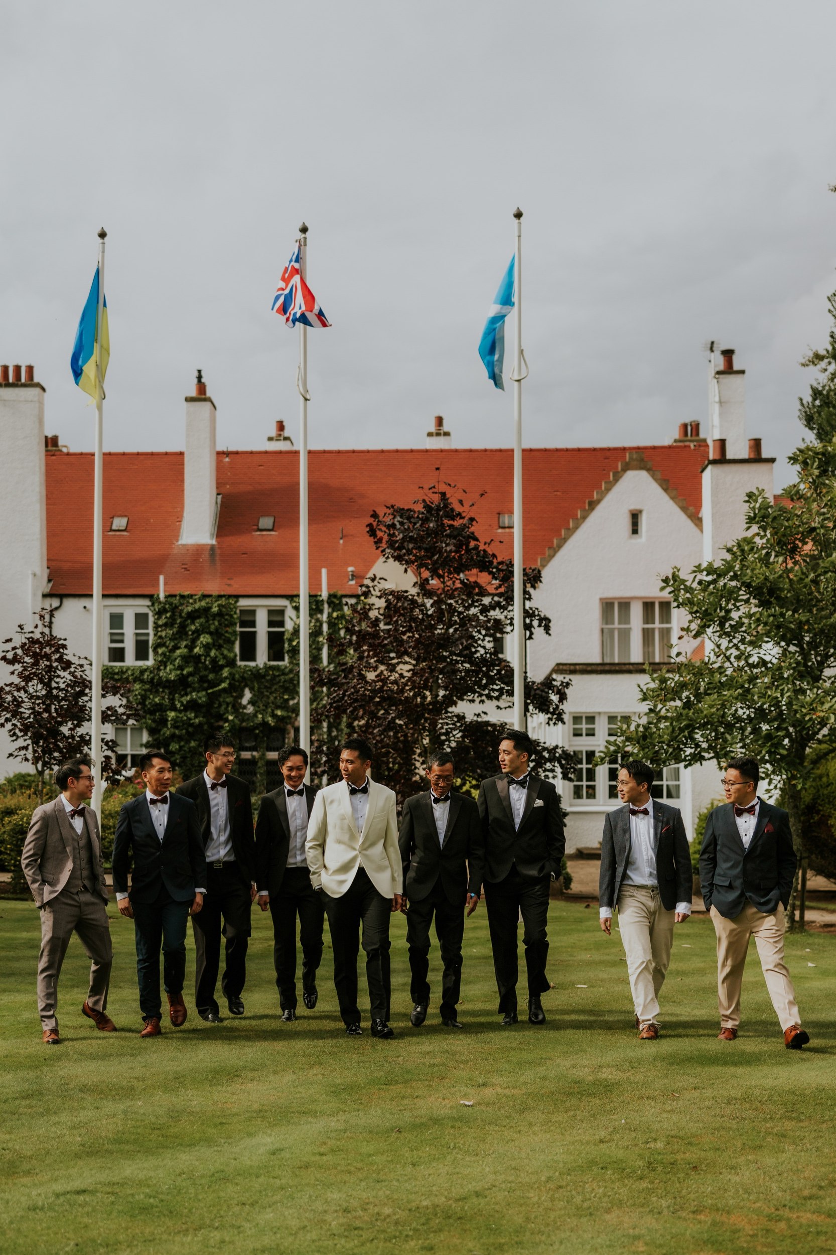 Gordon in a white dinner jacket walking with eight men across the lawn outside Lochgreen House Hotel.