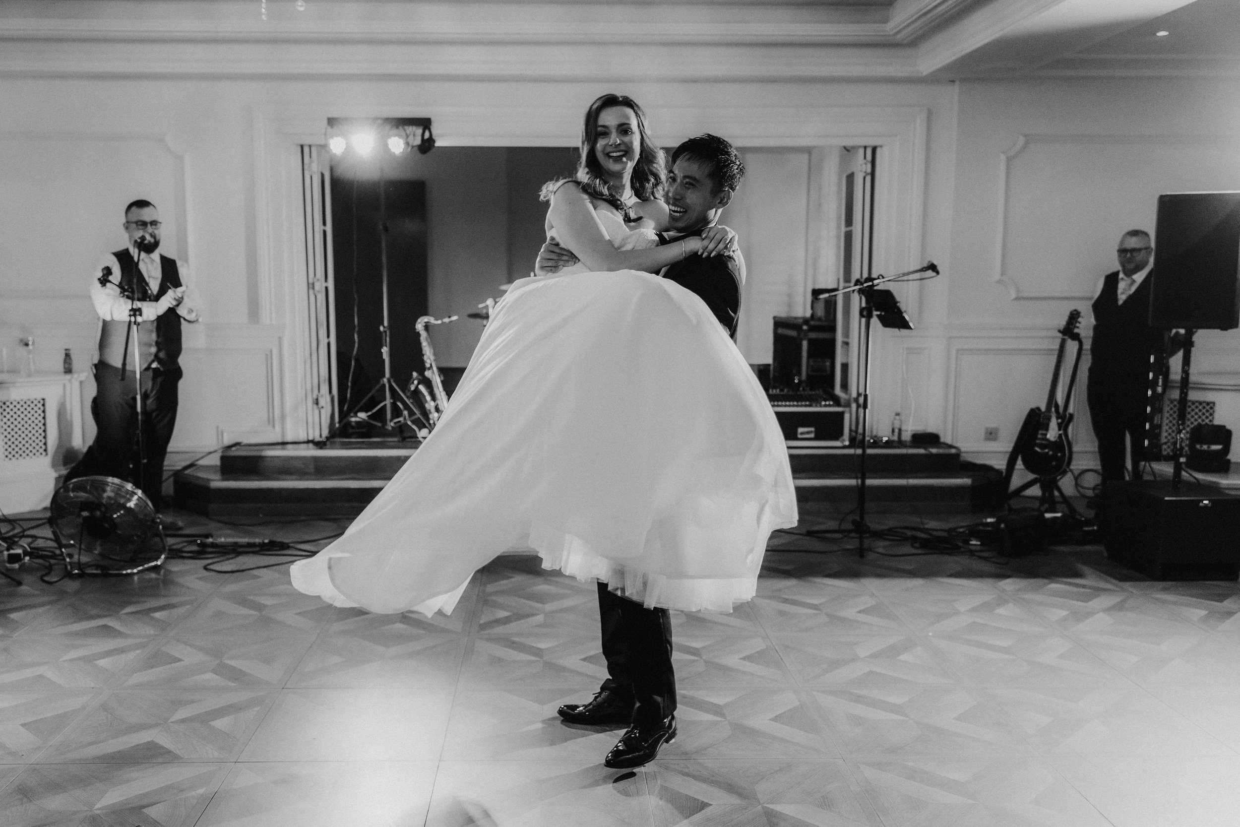 Gordon lifting Emma on the dance floor at Lochgreen House Hotel, with the band behind them, in black and white.