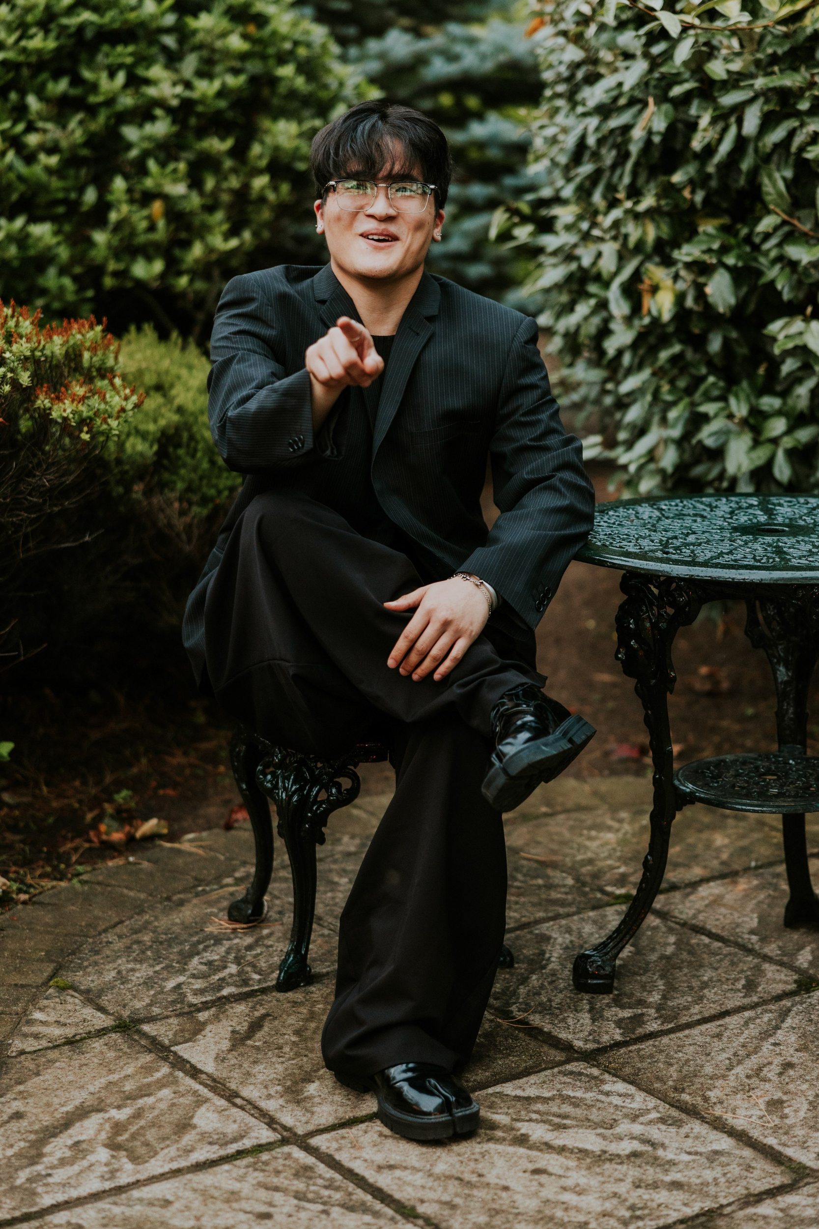 Guest in glasses and a dark pinstripe jacket smiling and pointing towards the camera beside a garden table.