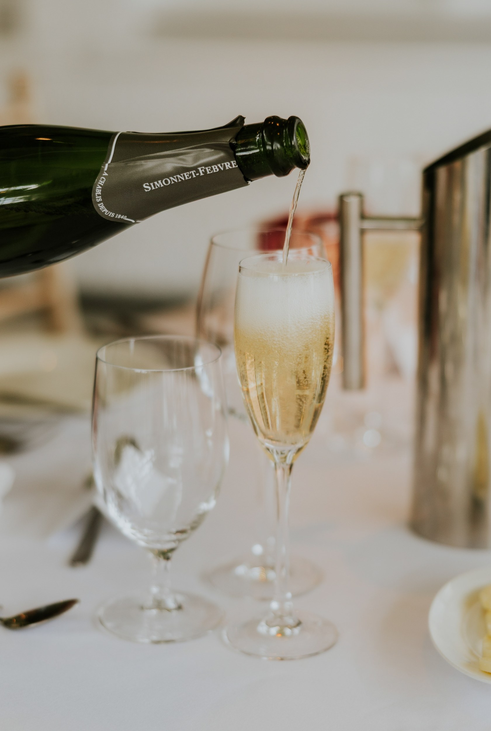 Sparkling wine being poured into a flute beside wine glasses and a metal jug at Lochgreen House Hotel.