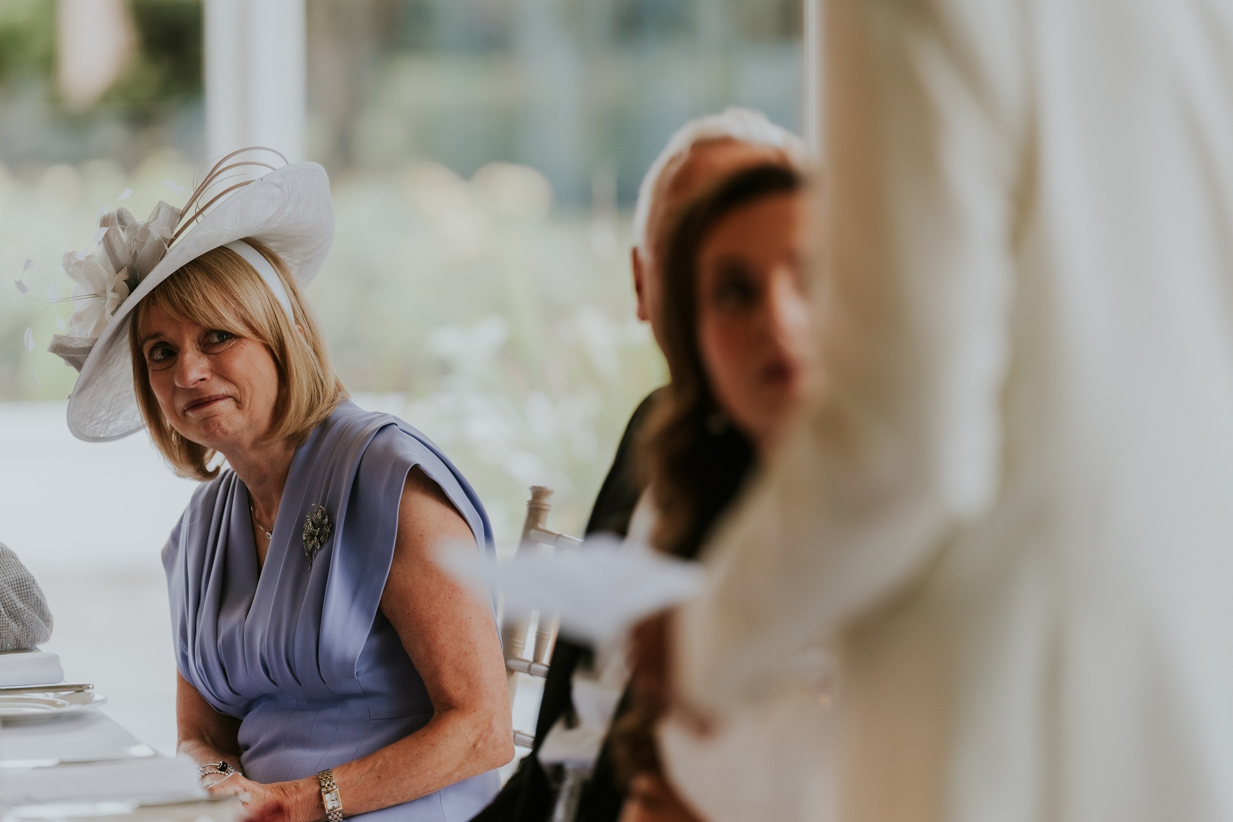 Wedding guest in a lilac dress and pale hat seated at a laid table at Lochgreen House Hotel.
