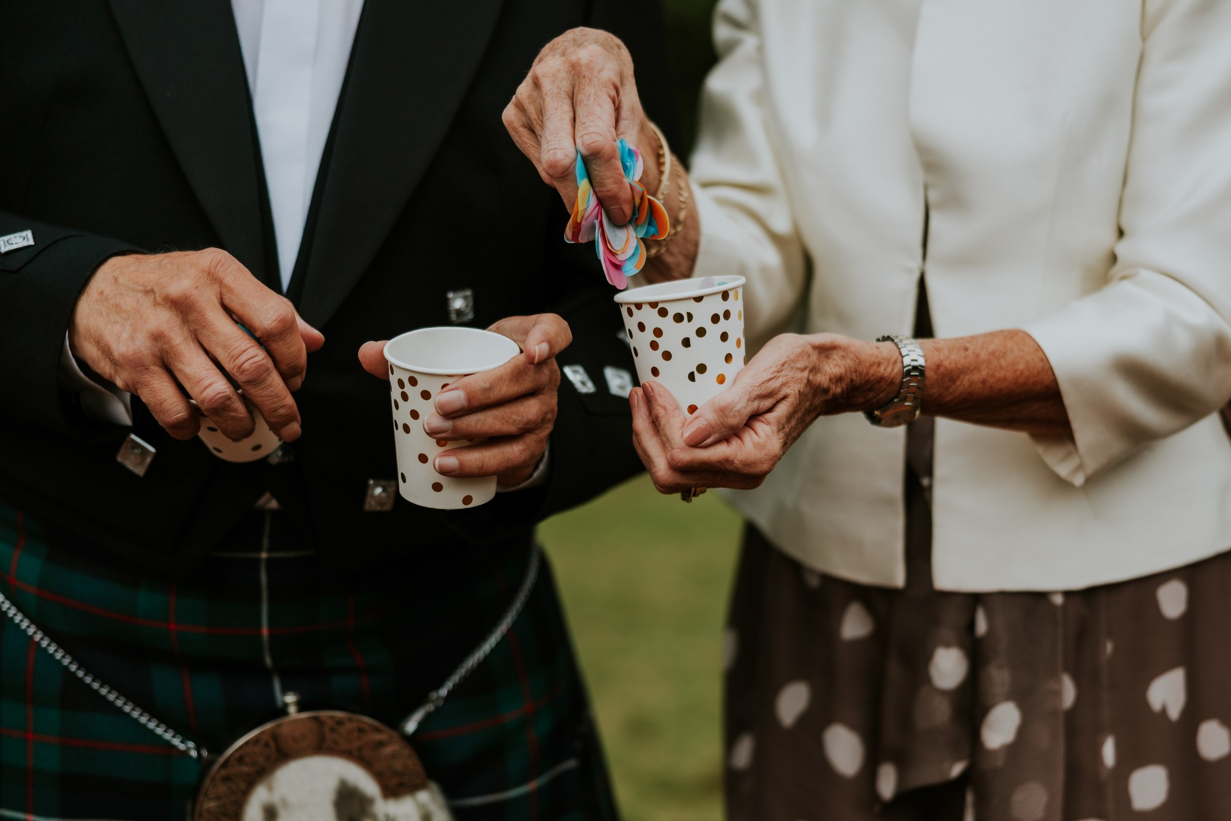 Wedding guests holding colourful confetti and gold-spotted paper cups.