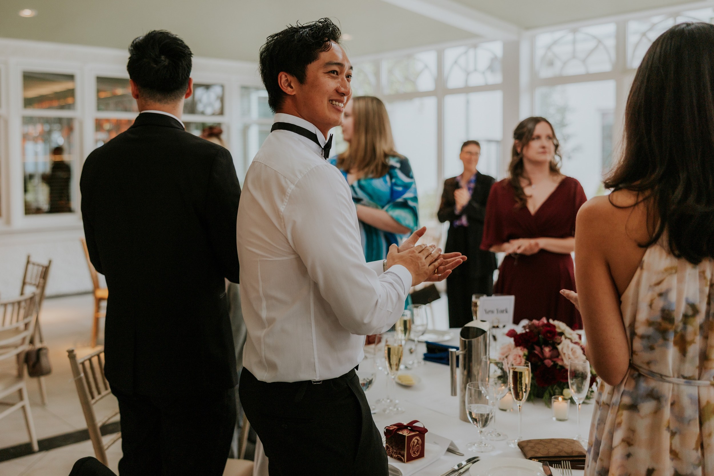 Wedding guests standing and applauding beside a decorated reception table at Lochgreen House Hotel.