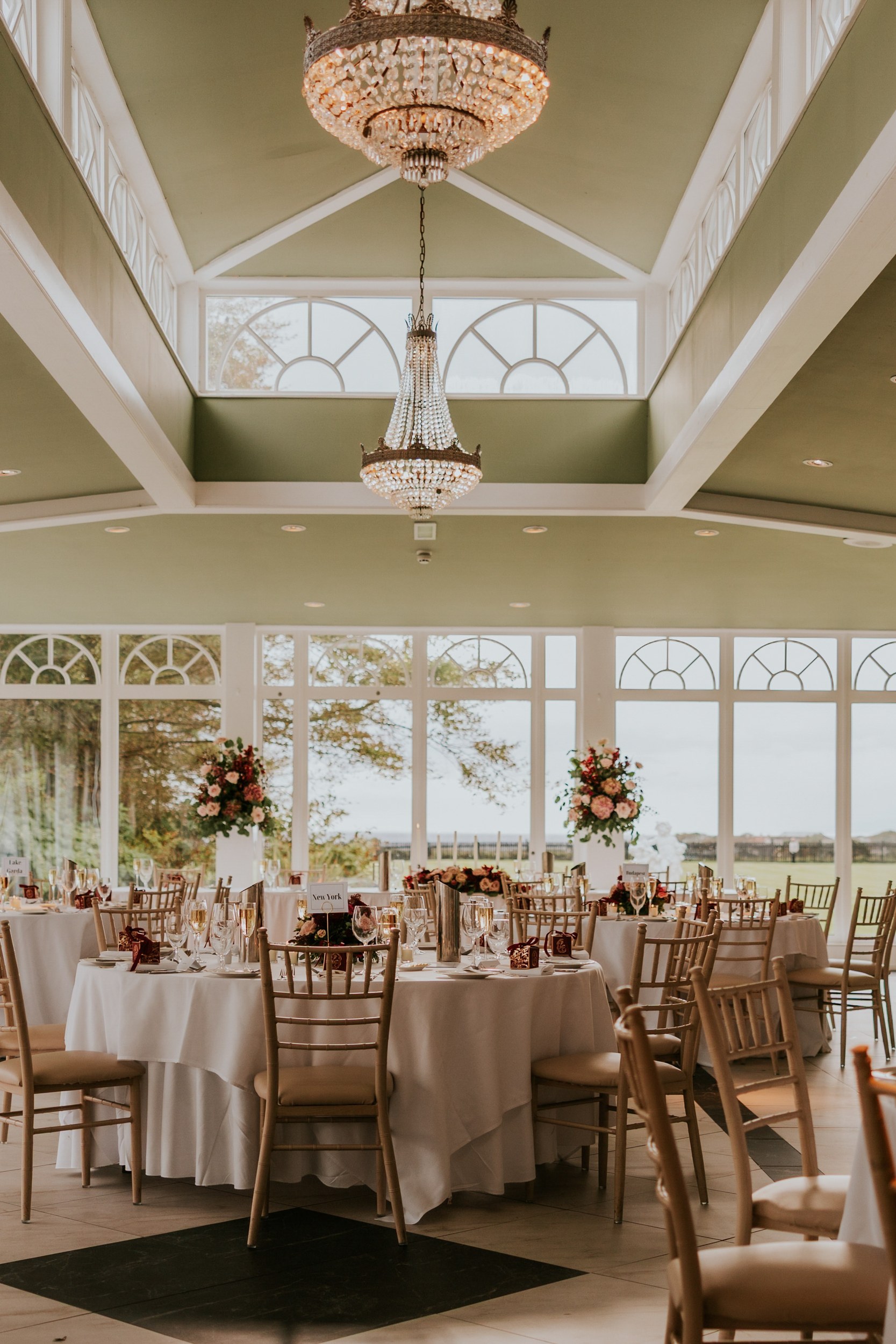 Wedding reception tables with floral centrepieces beneath crystal chandeliers at Lochgreen House Hotel.